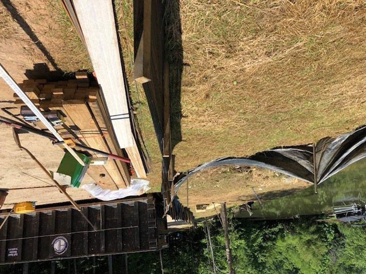 Stacked wooden planks beside a modern building exterior with grassy landscaping and plants
