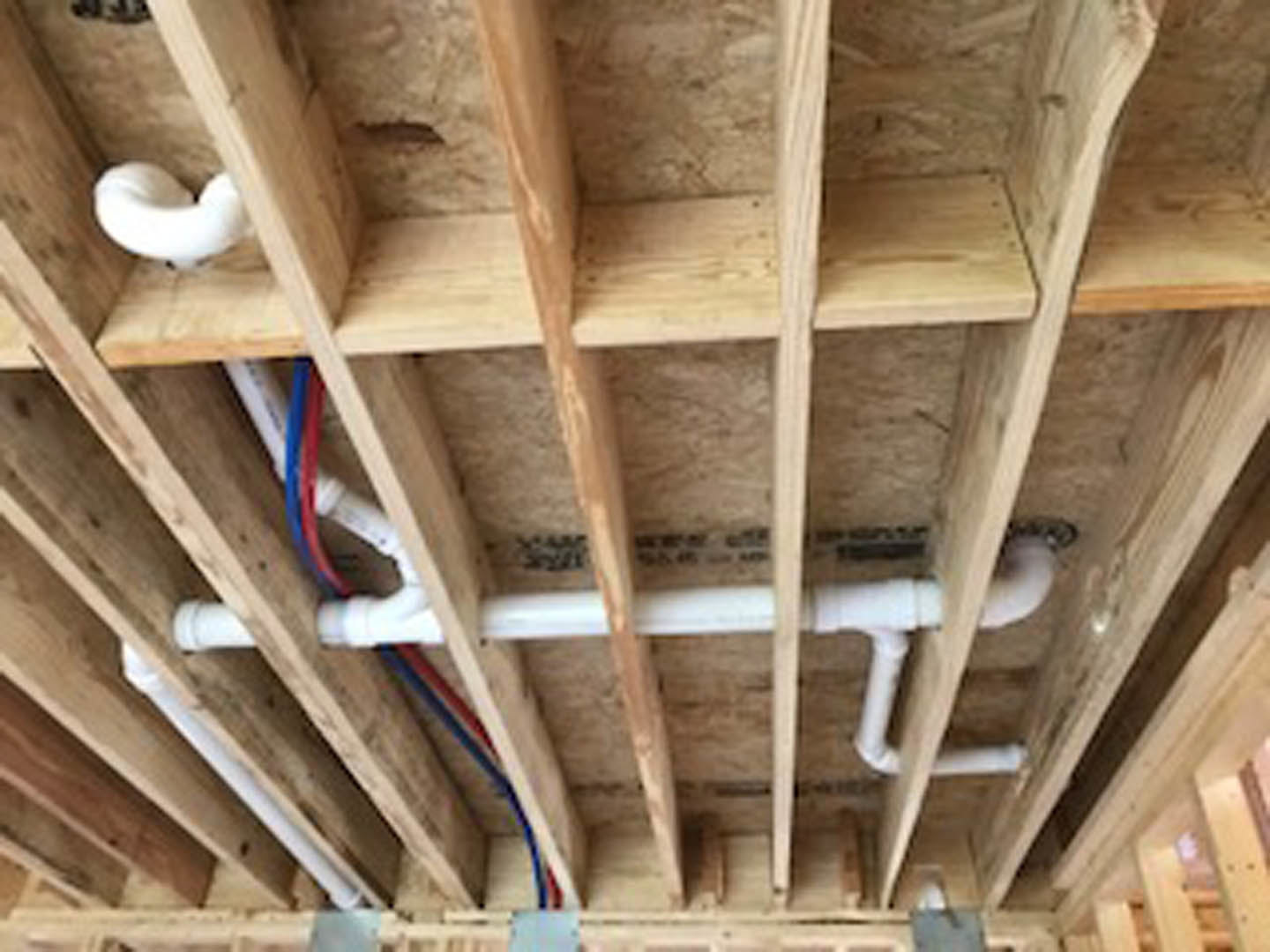 Exposed metal pipes running along unfinished wooden ceiling beams with visible plywood and insulation