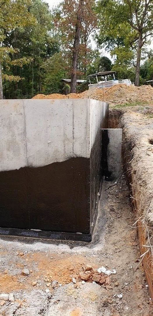 Concrete retaining wall bordered by loose dirt, red-leafed tree nearby, white vehicle with canopy parked in background