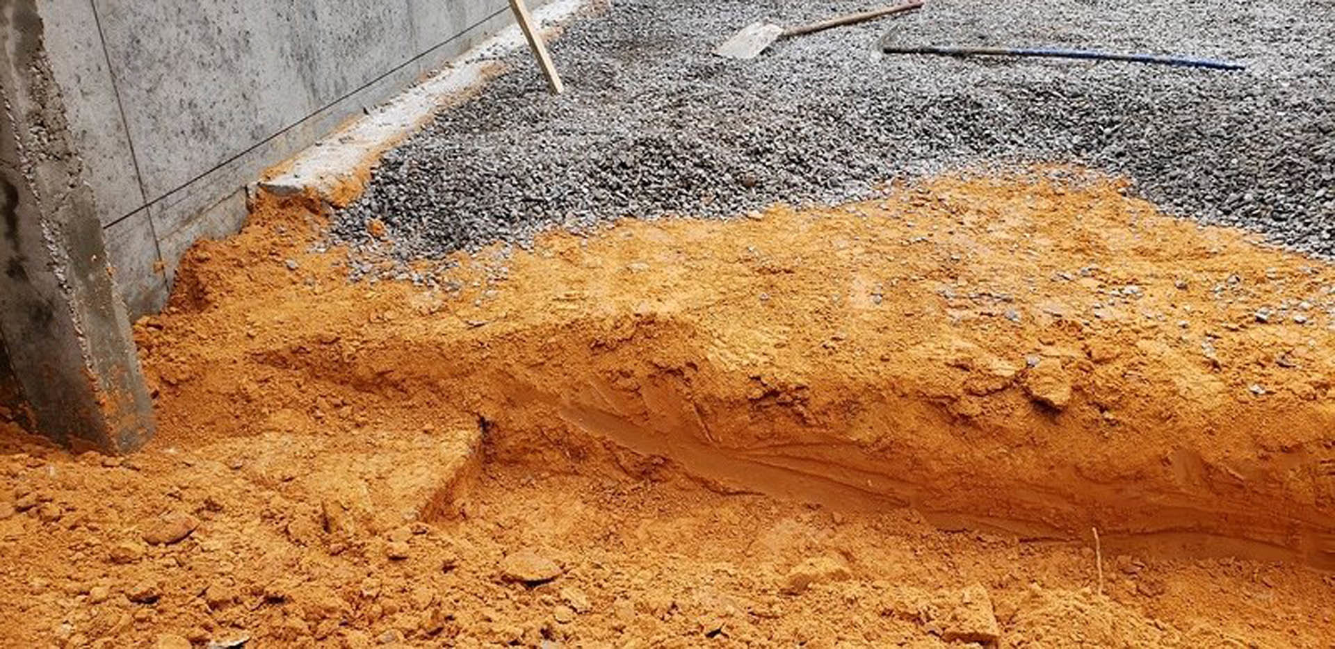 Large pile of gravel and dirt on bare outdoor ground, surrounded by soil and sparse vegetation