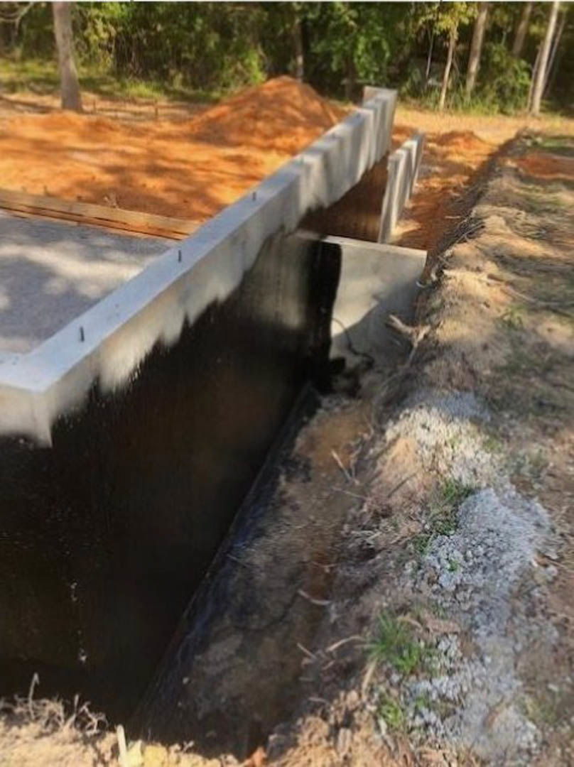 Concrete foundation under construction surrounded by dirt, with trees and grass in the background