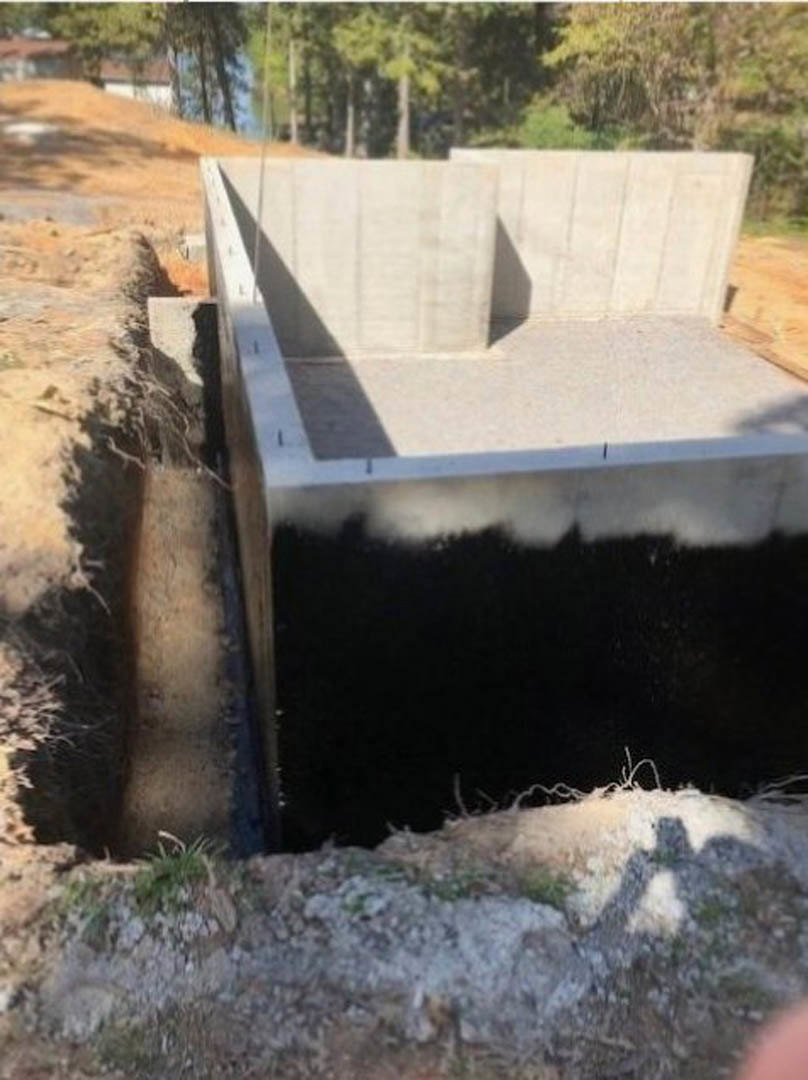 Concrete foundation set in an excavated dirt hole, surrounded by soil and outdoor elements.