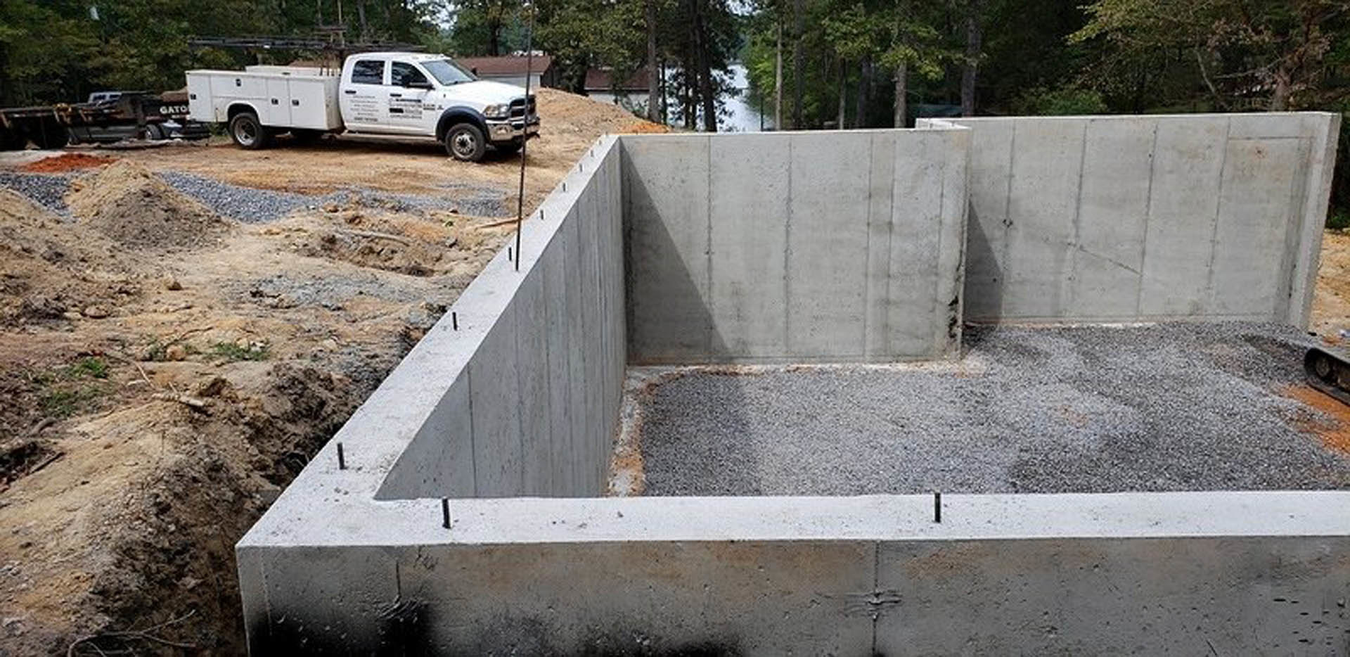 Concrete foundation slab surrounded by dirt and trees, white truck with attached white trailer parked in background