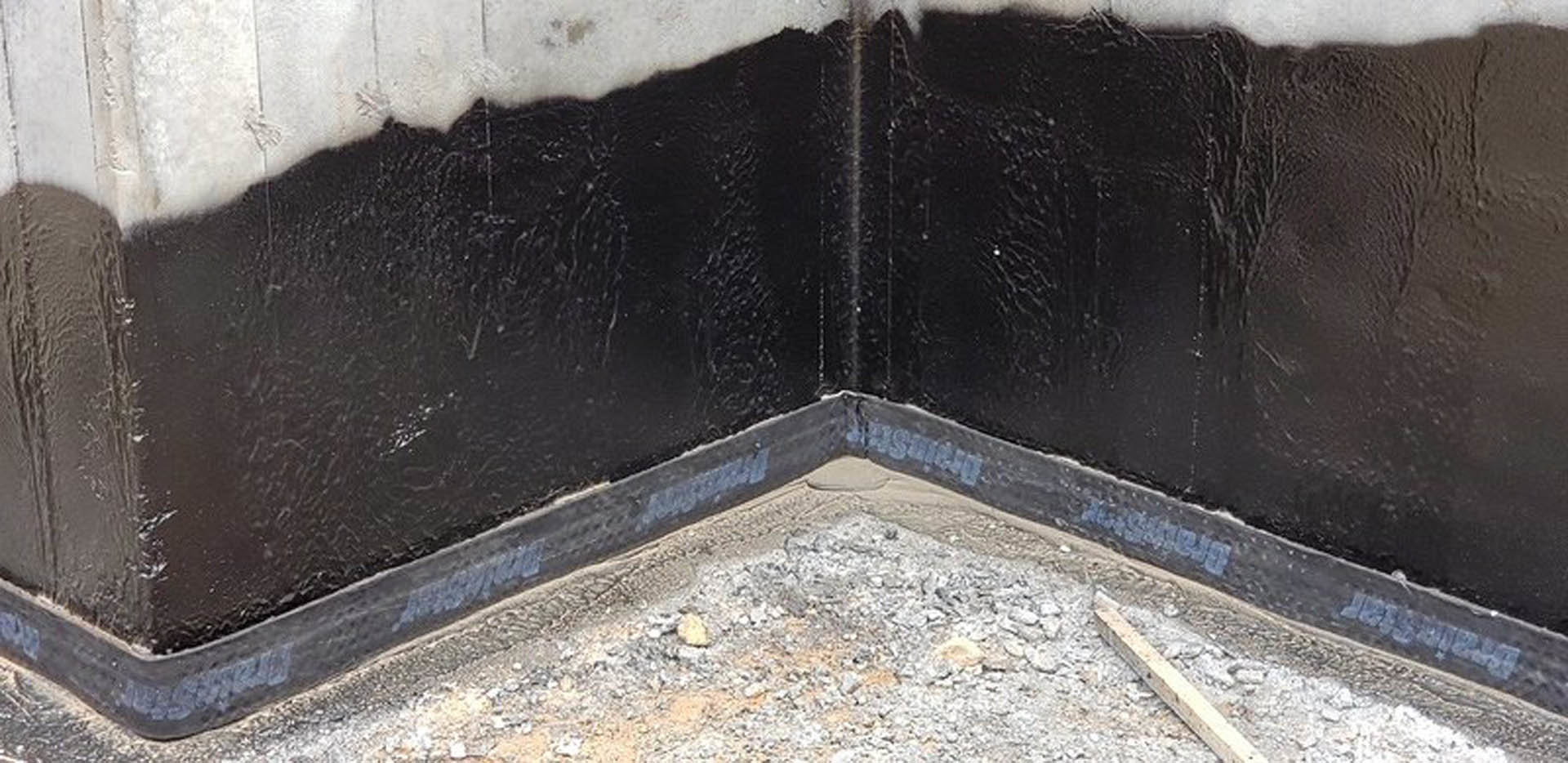 Black-painted corner of a residential building with concrete and composite materials, grey cement walls, and ground-level exterior finishes