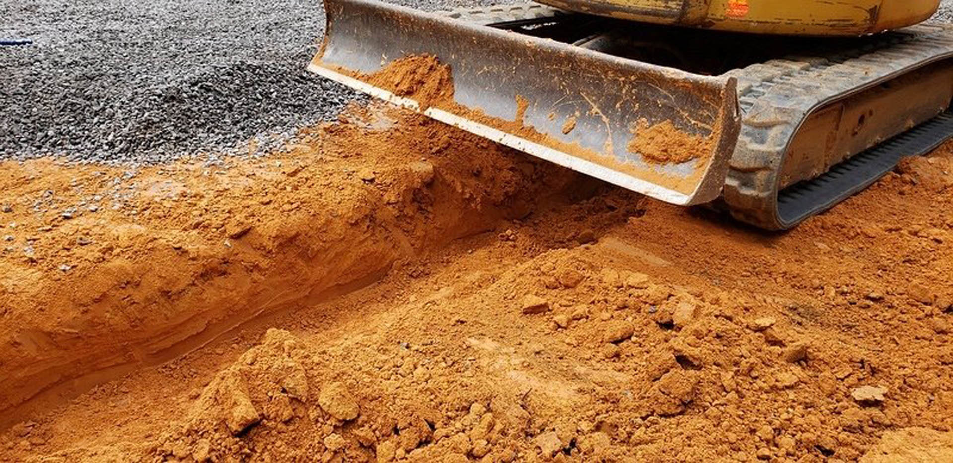 Loose soil and dirt covering the outdoor ground with a shovel nearby and a blurred red and yellow object in the background