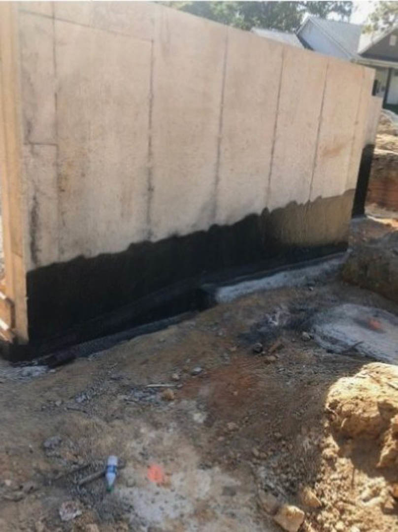 Concrete exterior wall with black and white paint, rough texture, adjacent to dirty ground and scattered rocks