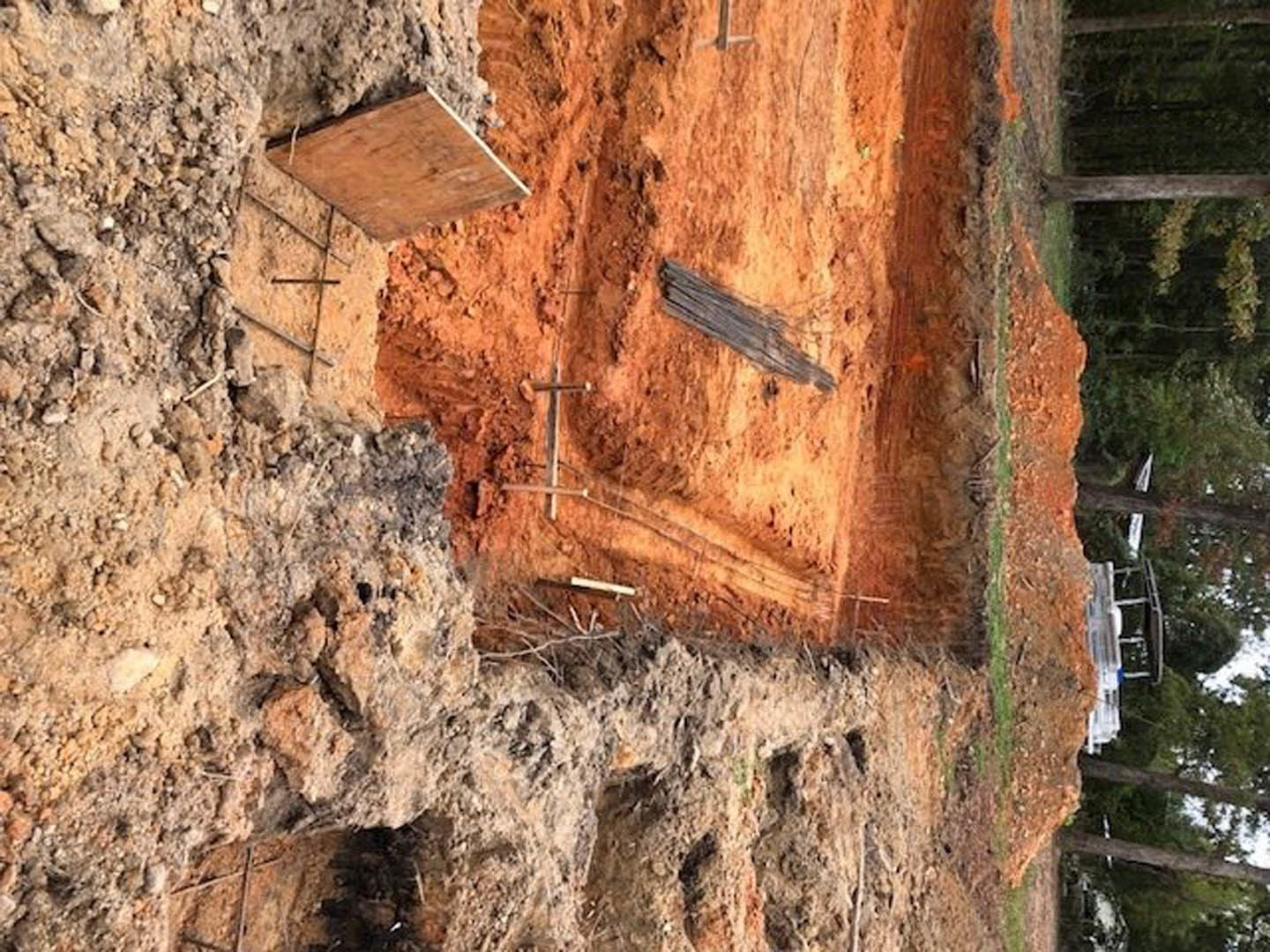 Dirt field bordered by a wooden fence, scattered rocks, and sparse trees in the background