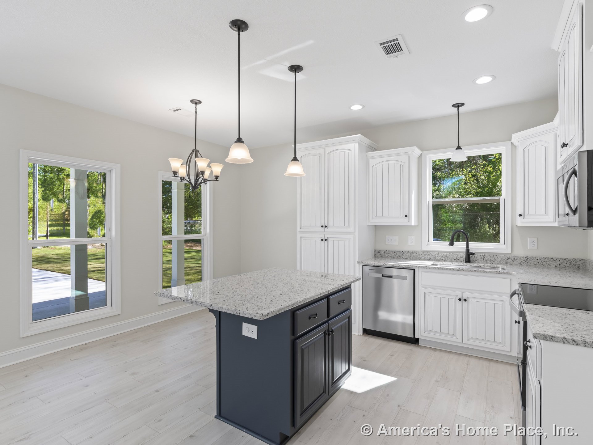 White shaker kitchen cabinets, granite island with built-in sink, stainless steel dishwasher and appliances, pendant and recessed lighting, large windows with decorative trim