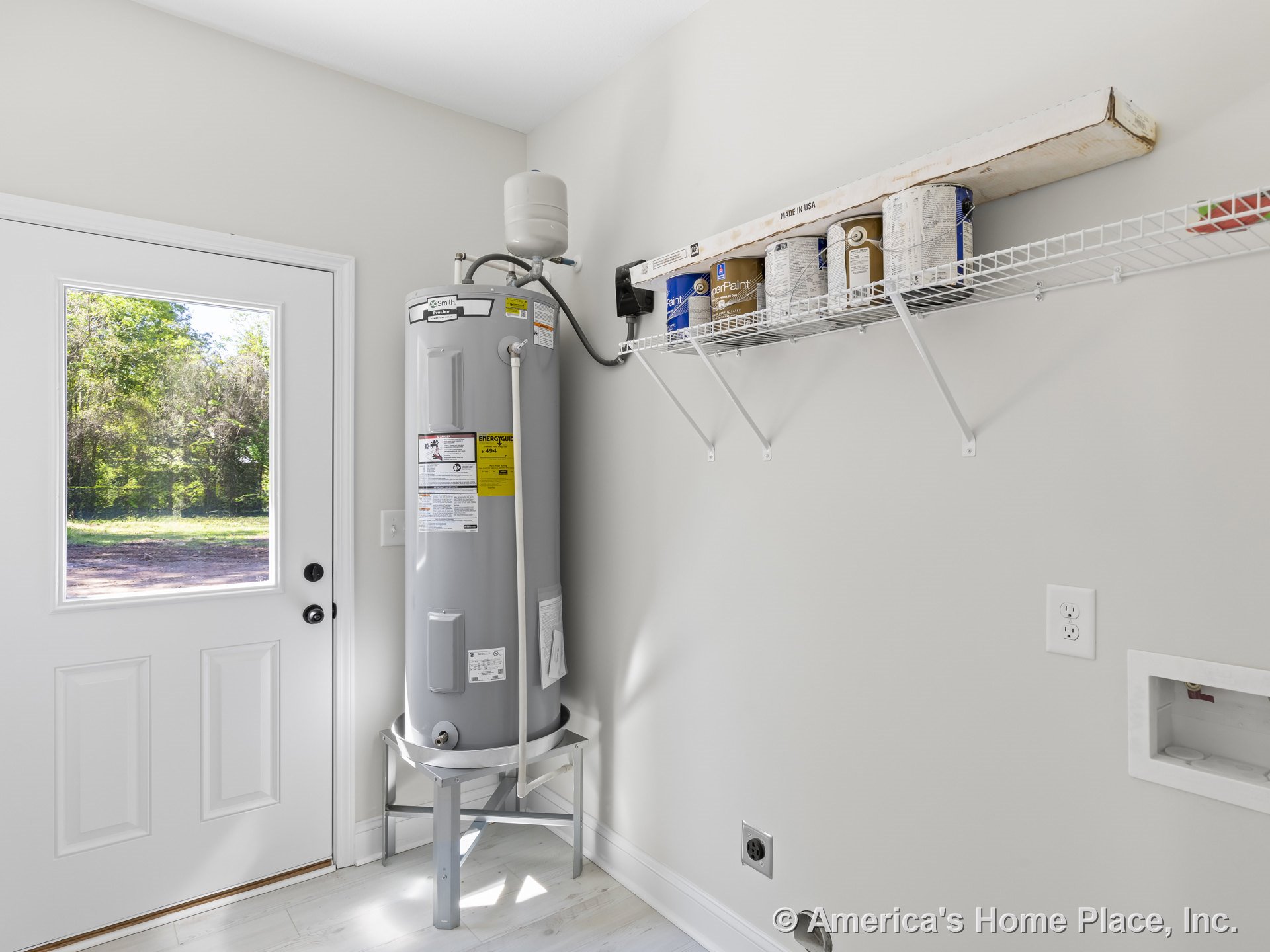 Laundry room with water heater, white wire shelving mounted above laundry hookups, exterior door with glass window, light vinyl plank flooring, neutral painted walls, wall trim