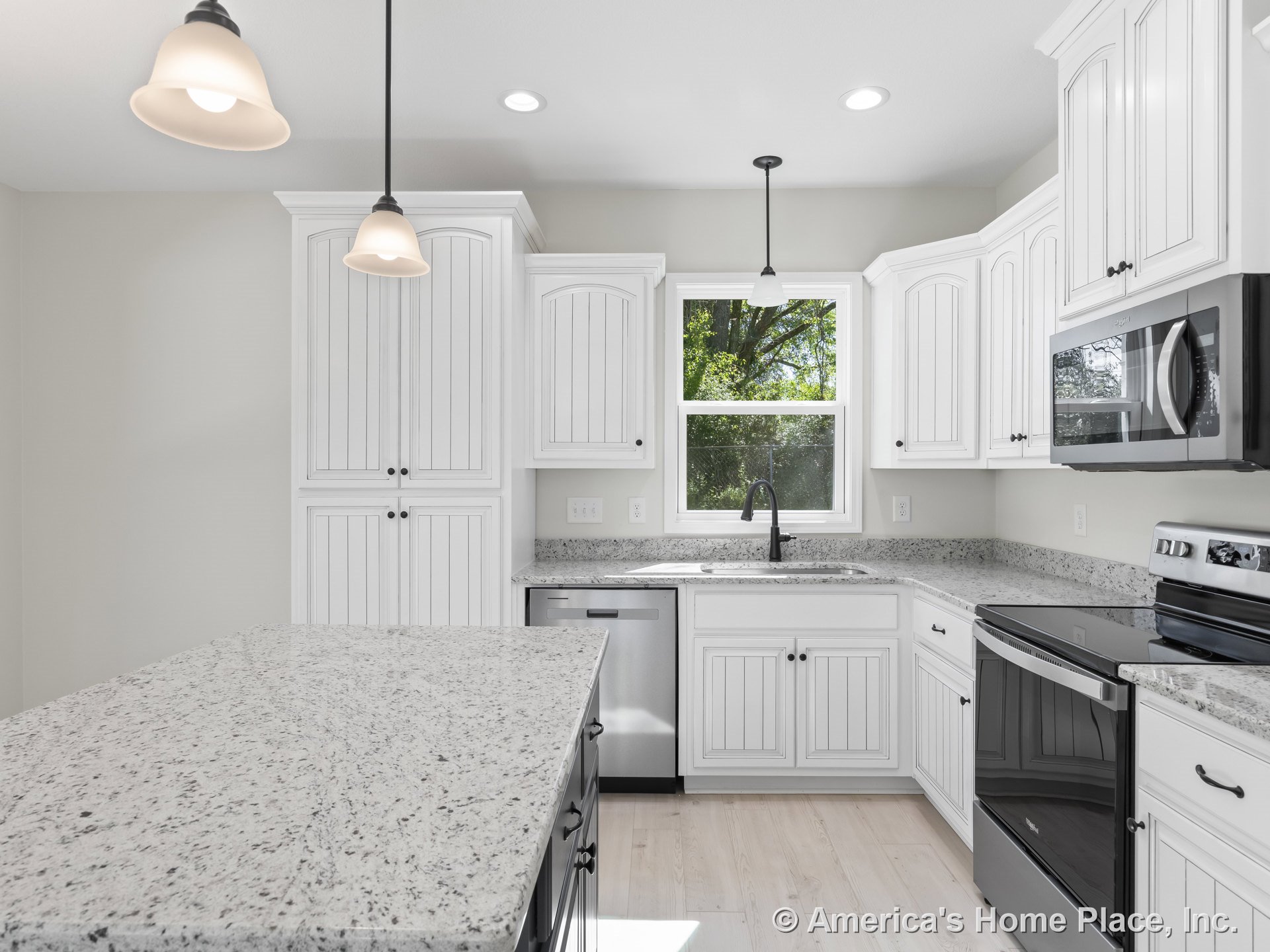 White beadboard kitchen cabinets with granite island countertop, stainless steel oven, built-in microwave, and dishwasher; double window above undermount sink; pendant and recessed
