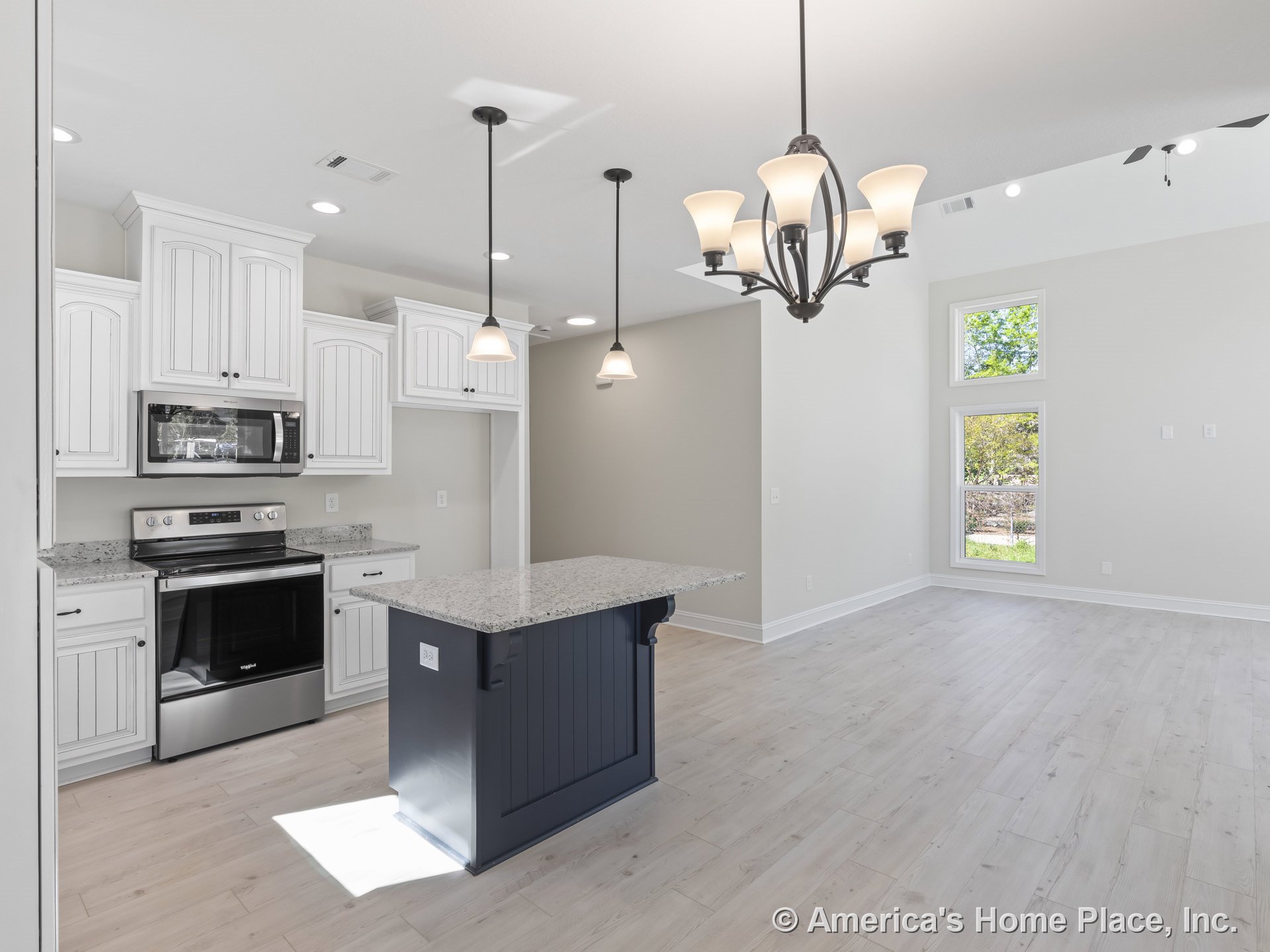 White upper and lower cabinets with granite countertops, dark blue central kitchen island featuring pendant lights, built-in stainless steel oven and microwave, light wood plank