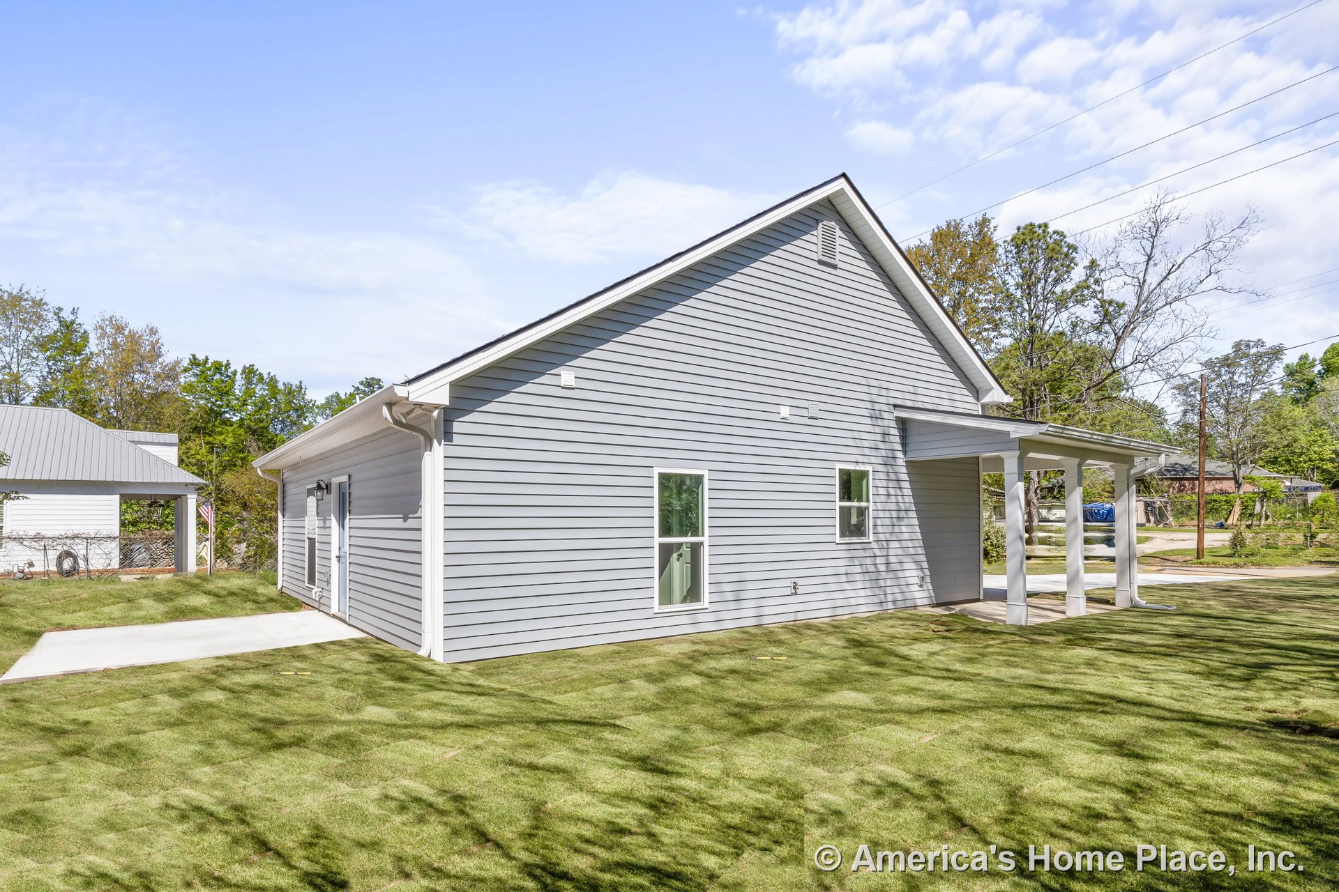 Gray horizontal vinyl siding exterior with covered side porch supported by white columns, double-hung windows, concrete patio, sloped roof, white trim, side entry, and landscaped