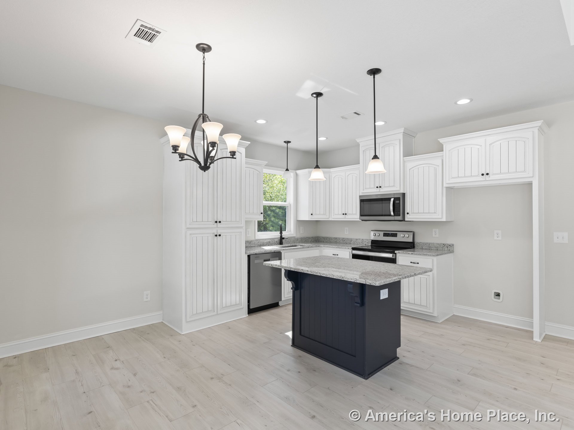 White beadboard cabinetry with granite countertops, central navy island topped with pendant lights, stainless steel appliances, light wood flooring, chandelier, and large windows