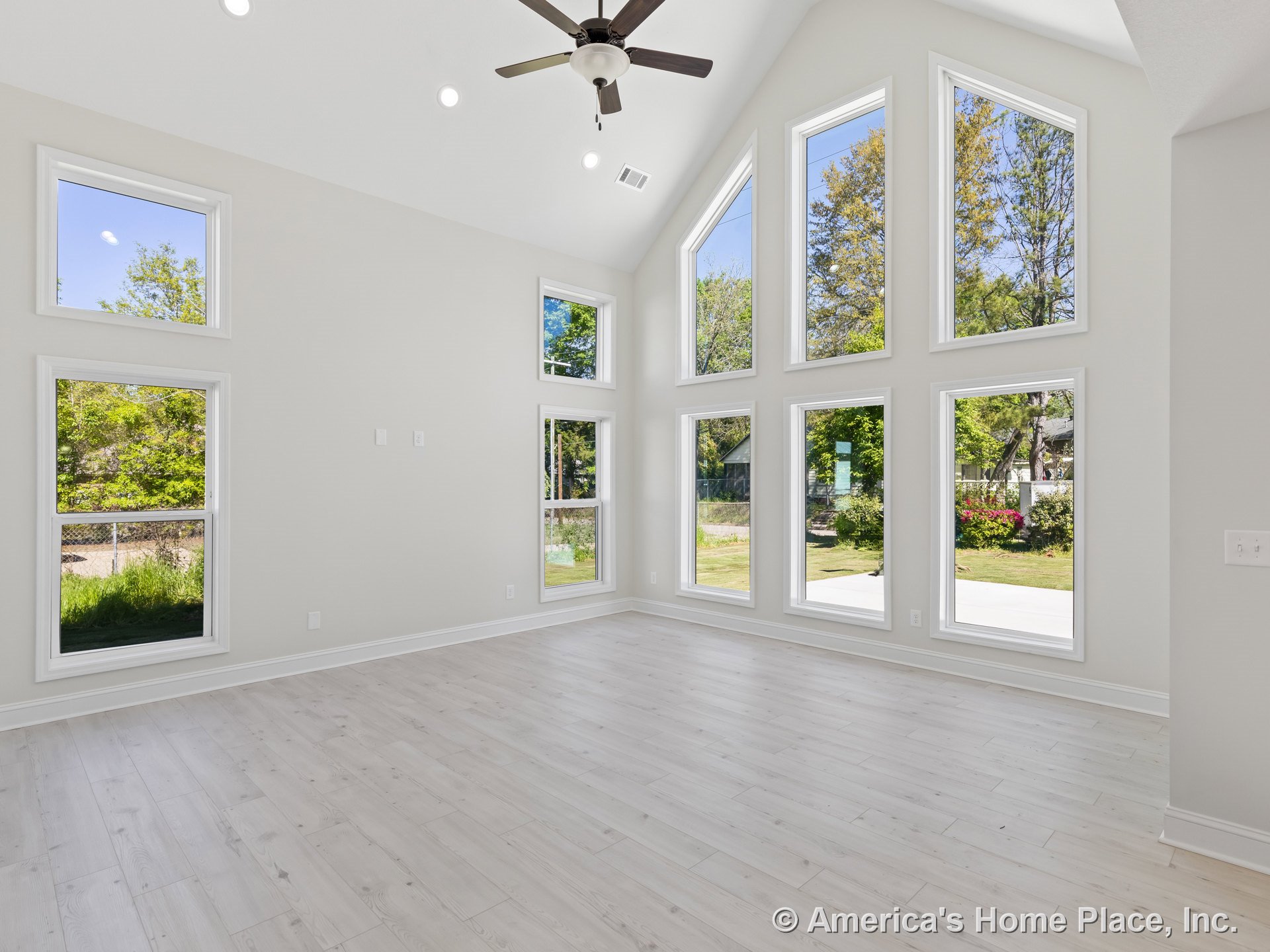 Vaulted ceiling with recessed lighting and ceiling fan, wall of tall windows providing backyard views, light wood flooring, white trim and baseboards, neutral wall color, open
