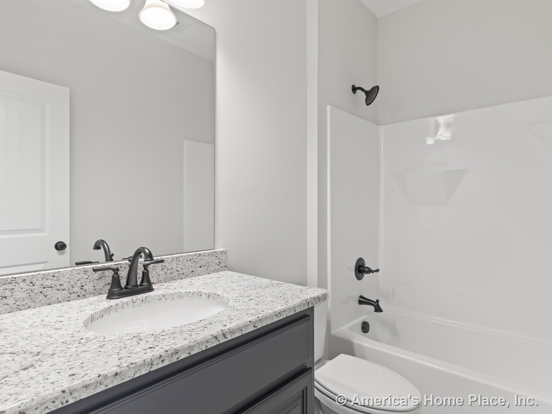Granite vanity countertop with dark wood cabinetry, white built-in bathtub featuring matte black faucet and shower fixtures, large wall mirror, overhead built-in lighting, and tile