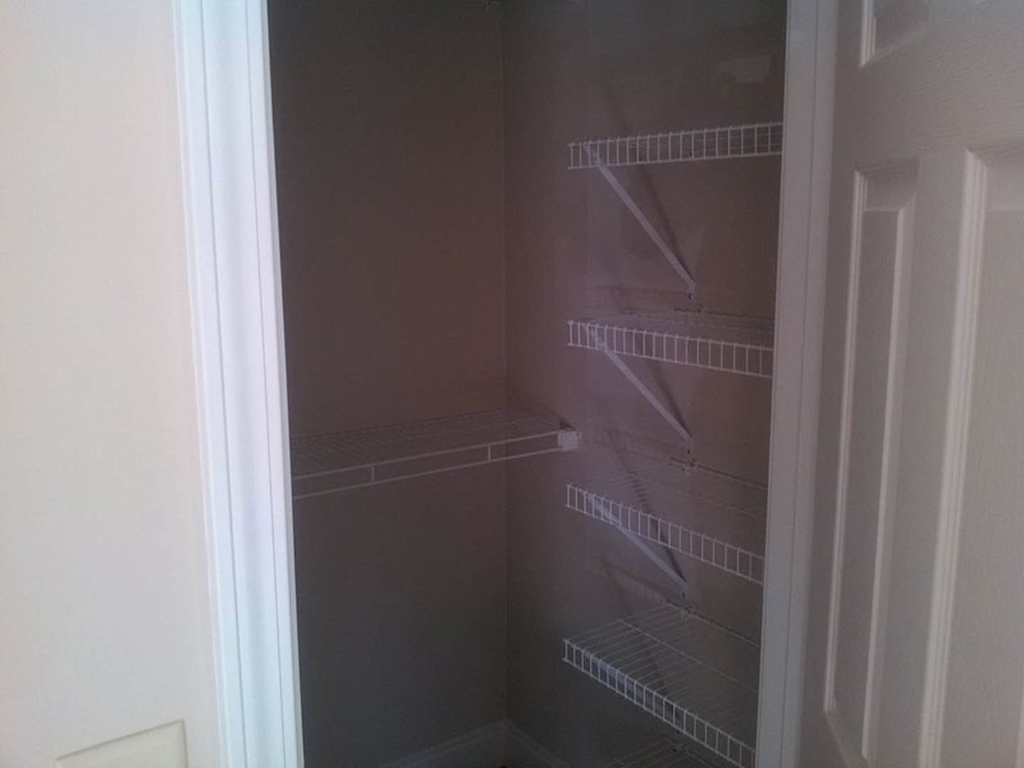 White closet interior with built-in metal shelving and white bars, adjacent to plastered walls and a door.