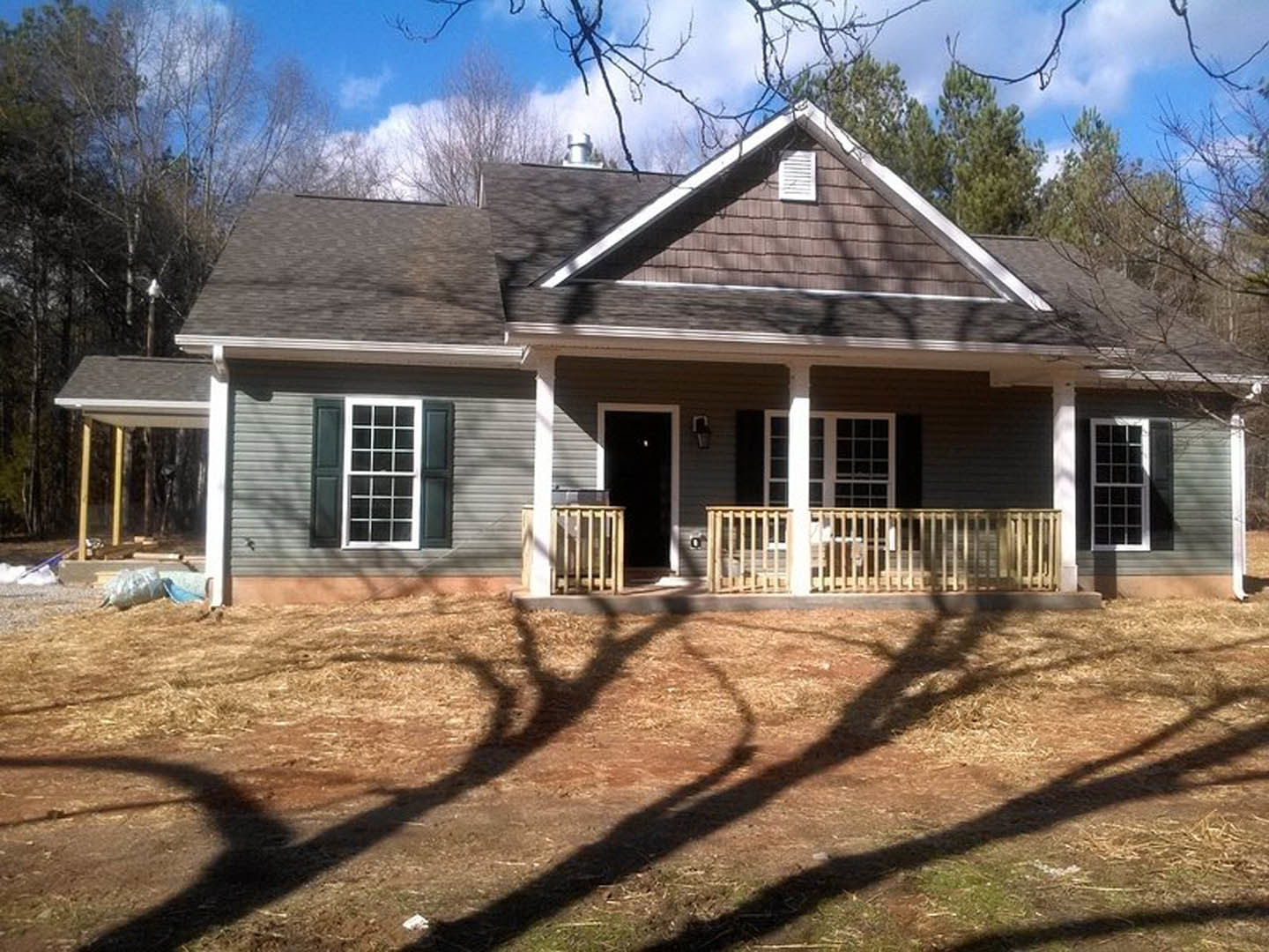 Brick house with covered porch, black front door, white-framed windows, tree in backyard casting shadow on lawn