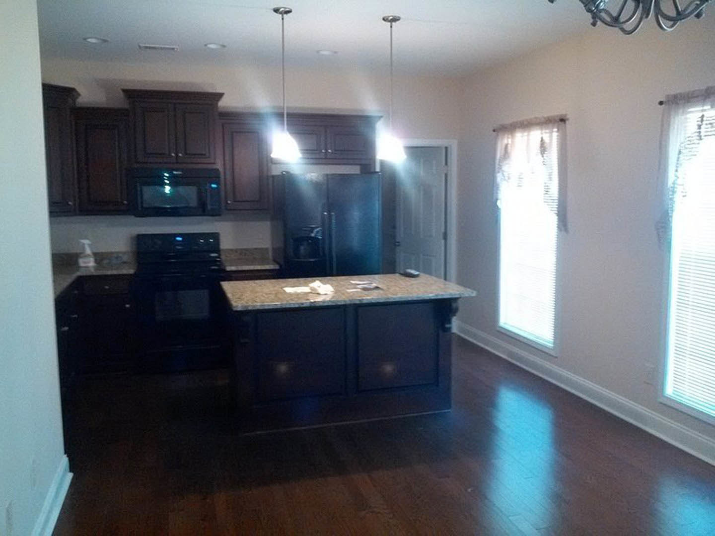 Kitchen with dark wood cabinets, granite island countertop, stainless steel appliances, and window with white blinds letting in sunlight