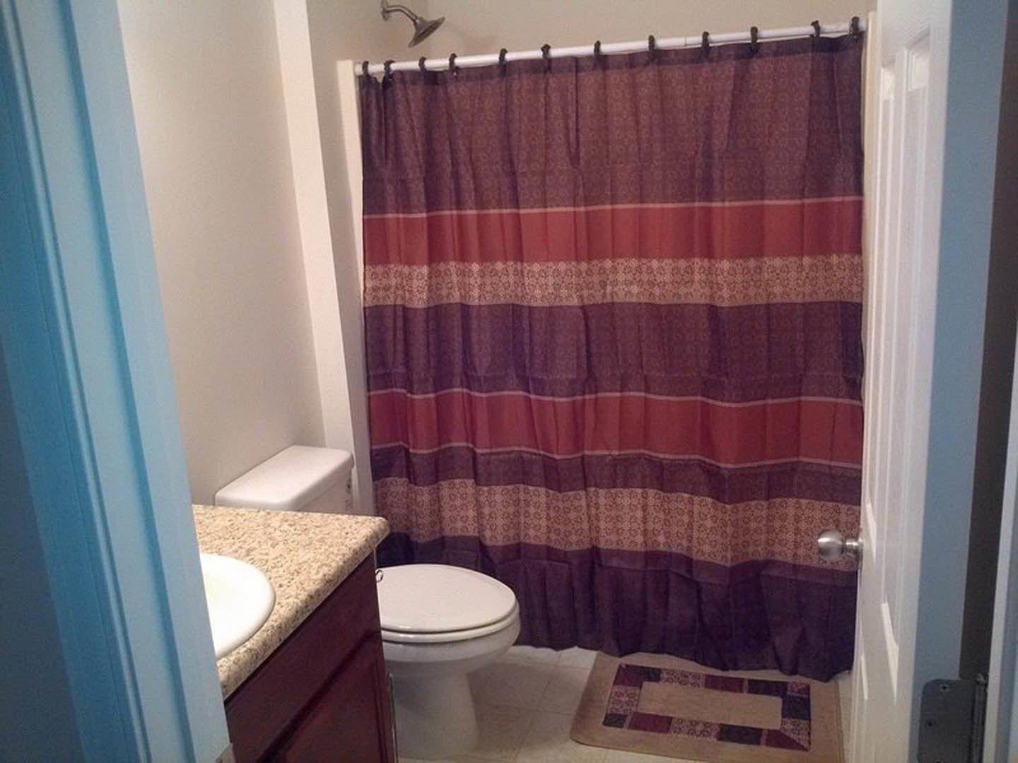 Bathroom with white tile walls, striped fabric shower curtain, white toilet with closed lid, and chrome faucet on a white sink