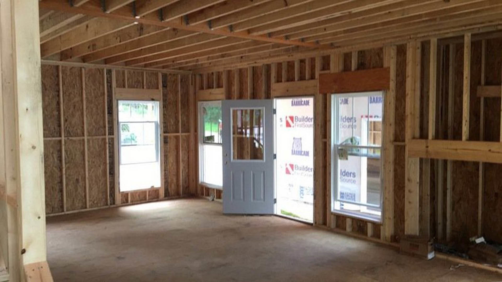 Wood-beamed ceiling above hardwood floors, glass door and large windows letting in natural light, neutral walls, modern interior finishes