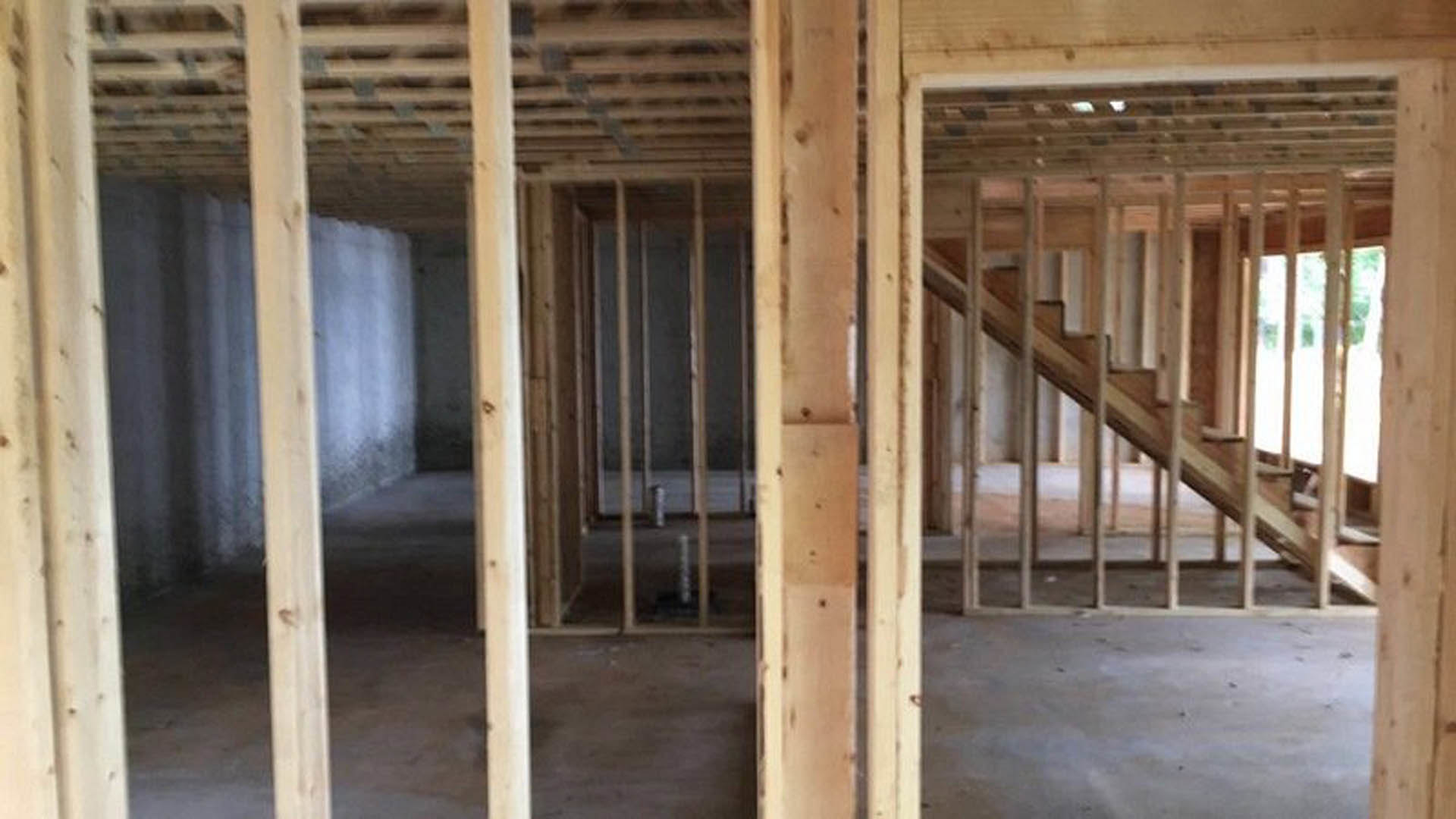 Unfinished interior with exposed wooden beams, central staircase framed by lumber, visible wall insulation, and construction materials scattered on subfloor