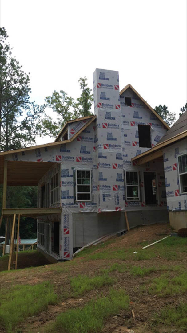Two-story house with brick chimney, white-framed windows, black front door displaying a red and white sign, surrounded by grass and trees under a blue sky
