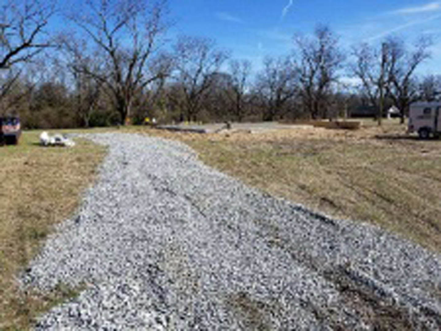 Gravel path winding through grassy field, bordered by leafless trees and patches of exposed earth under open sky
