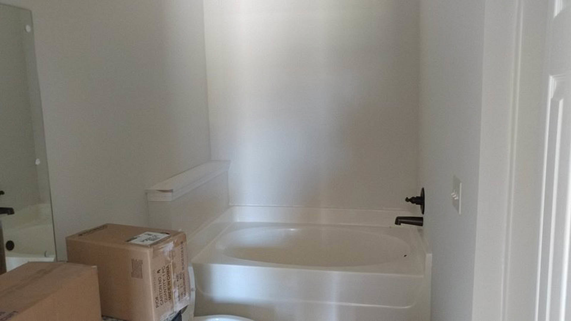 Modern bathroom featuring a freestanding white tub, wall-mounted toilet, light gray tile flooring, and smooth plaster walls with chrome fixtures