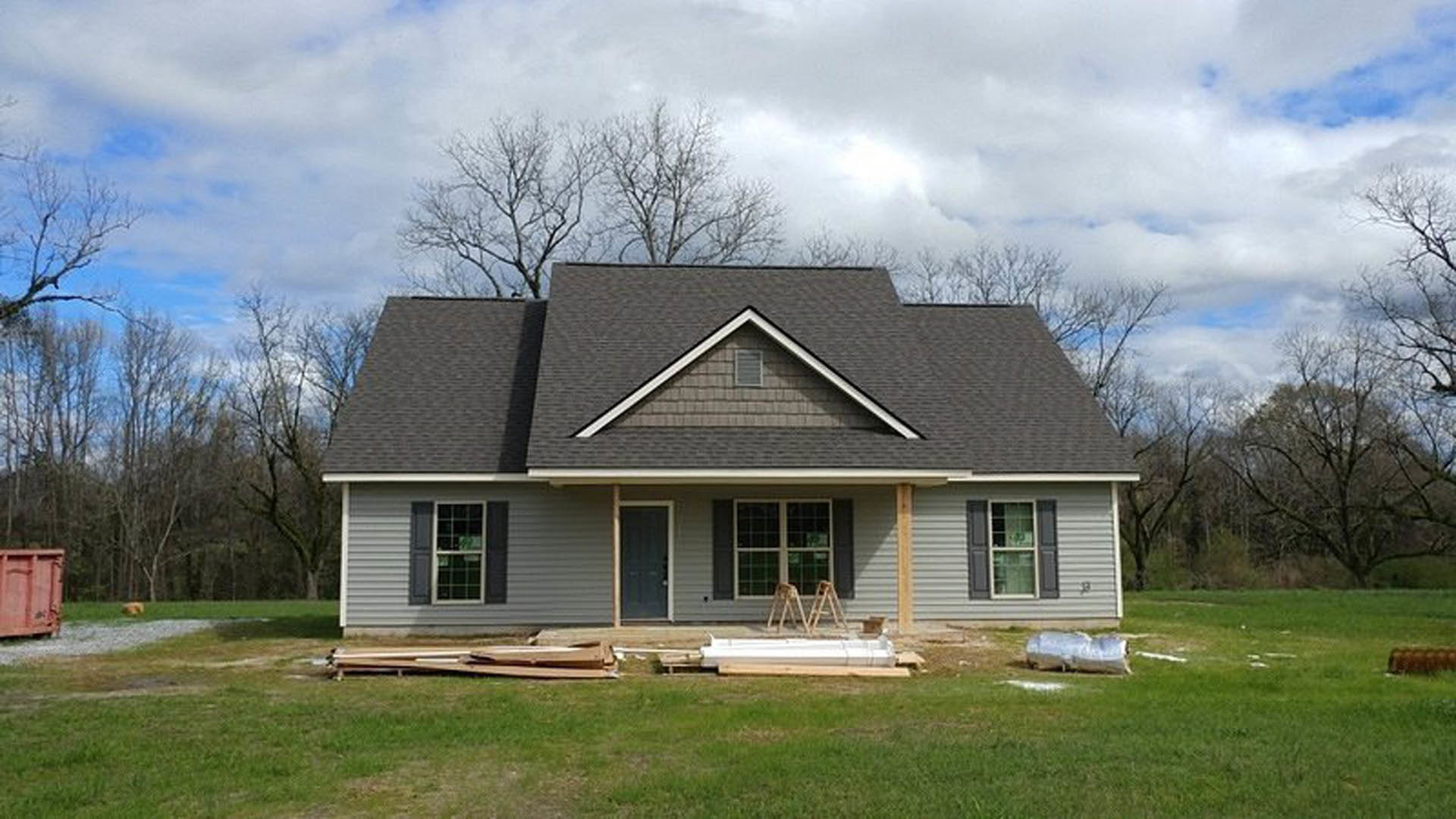 Modern cottage-style home with white siding, dark roof, small porch, wooden ladder leaning against exterior, green grass lawn, and white-framed windows.