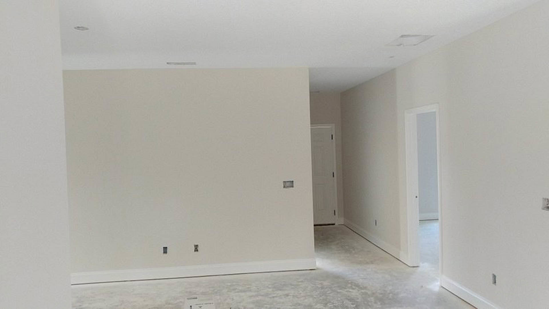 White-walled room with white paneled door featuring a black handle, smooth plaster surfaces, and light-colored flooring.