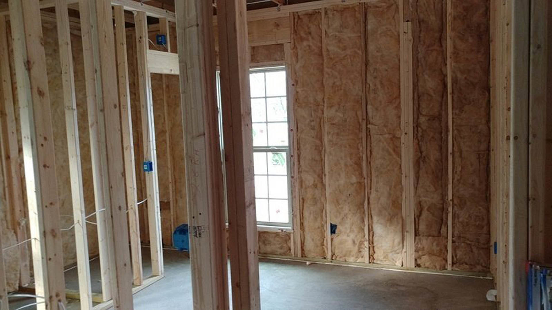 Wood-paneled room with a white-framed window, exposed insulation on one wall, and hardwood plank finishes