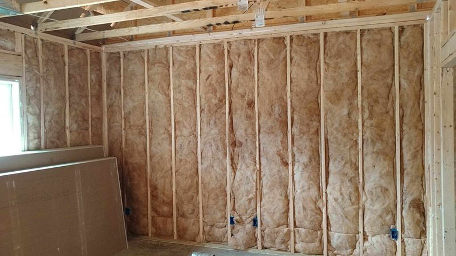 Exposed plywood wall with vertical wood beams and black electrical wires, unfinished interior remodel