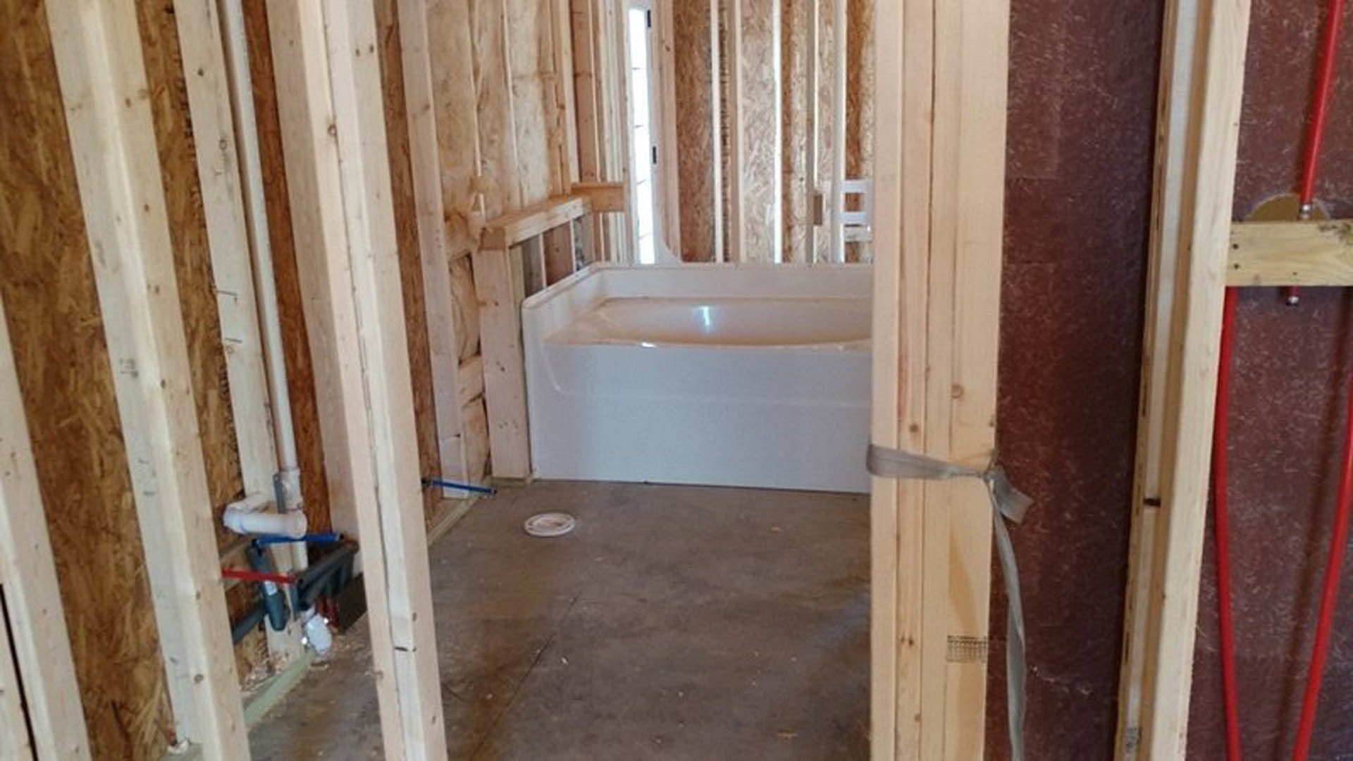 Freestanding white bathtub centered on wood plank flooring, surrounded by plaster walls, large window in background, minimal decor