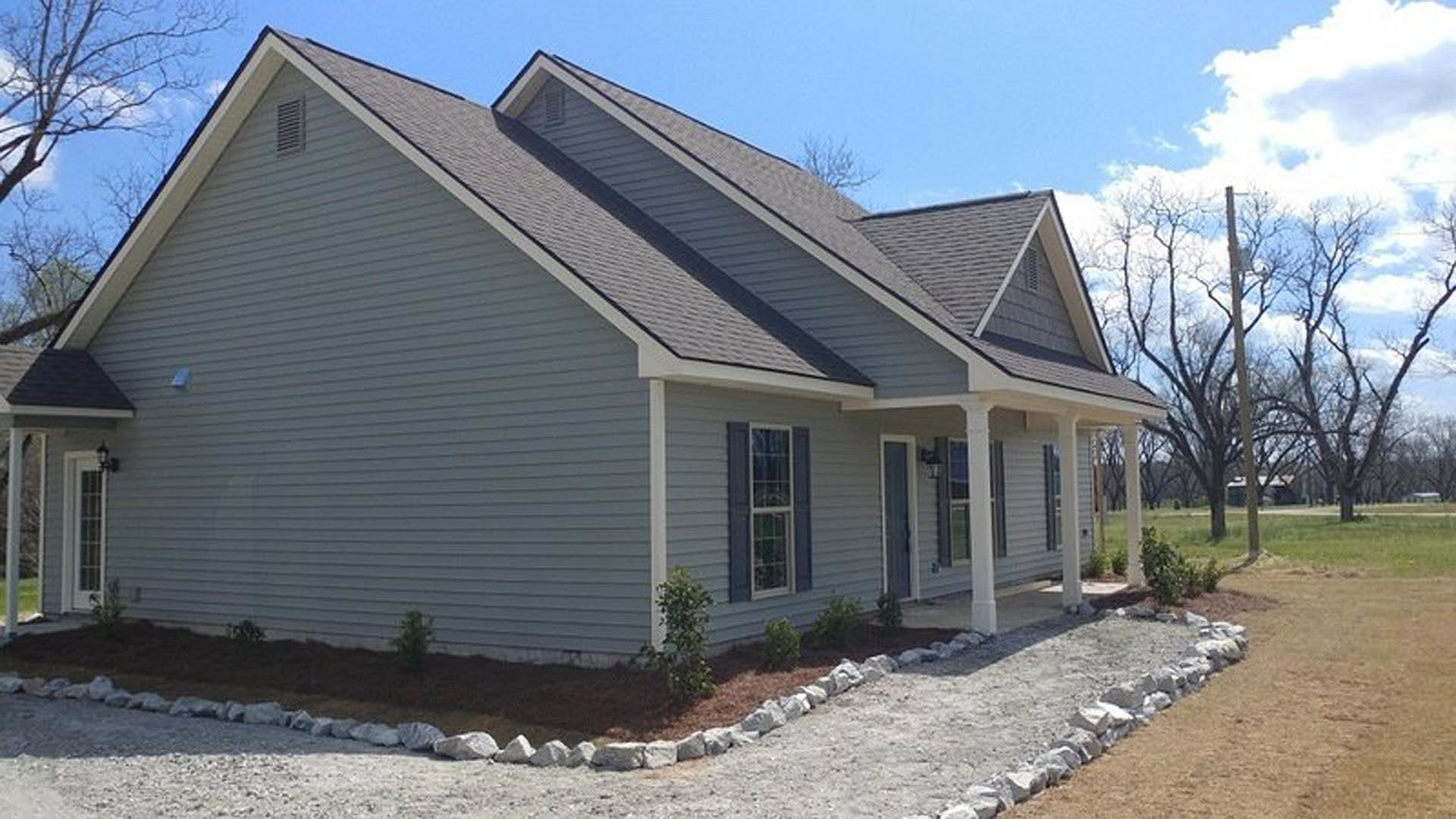 Two-story home with white roof, white-framed windows, stone border along foundation, paved driveway, and mature tree in front yard
