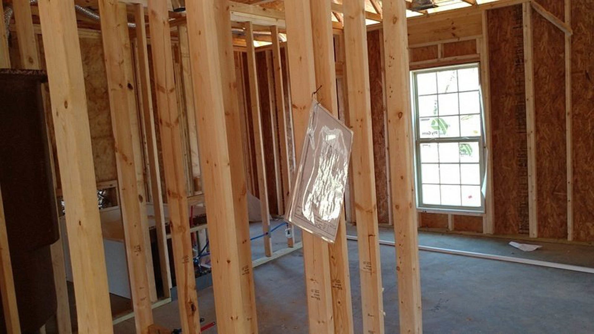 Exposed wooden framing with vertical and horizontal beams, unfinished interior, visible lumber and building insulation