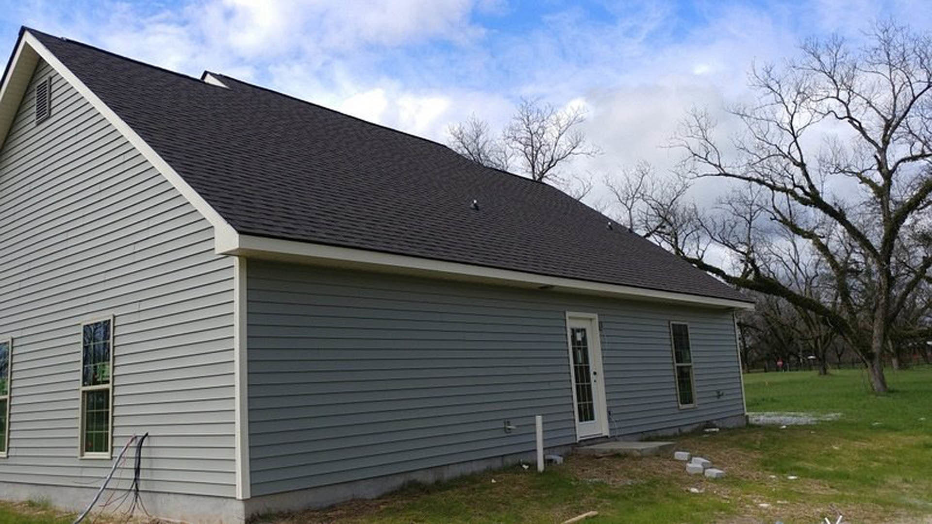 Two-story home with light siding, gabled roof, front lawn, leafless tree, and blue sky with scattered clouds