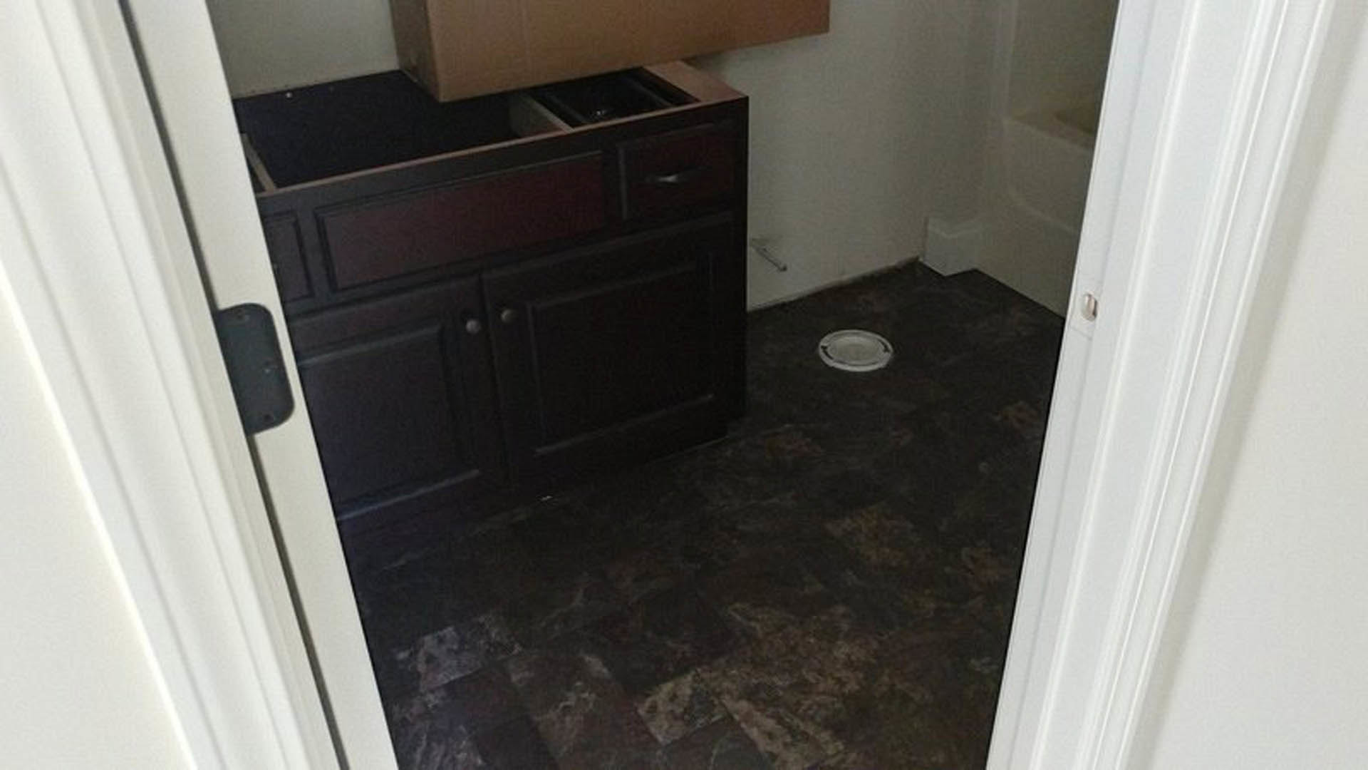 Modern bathroom featuring a white sink atop a wood vanity, drawer partially open revealing a rectangular storage box, light-colored tile flooring, and neutral painted walls