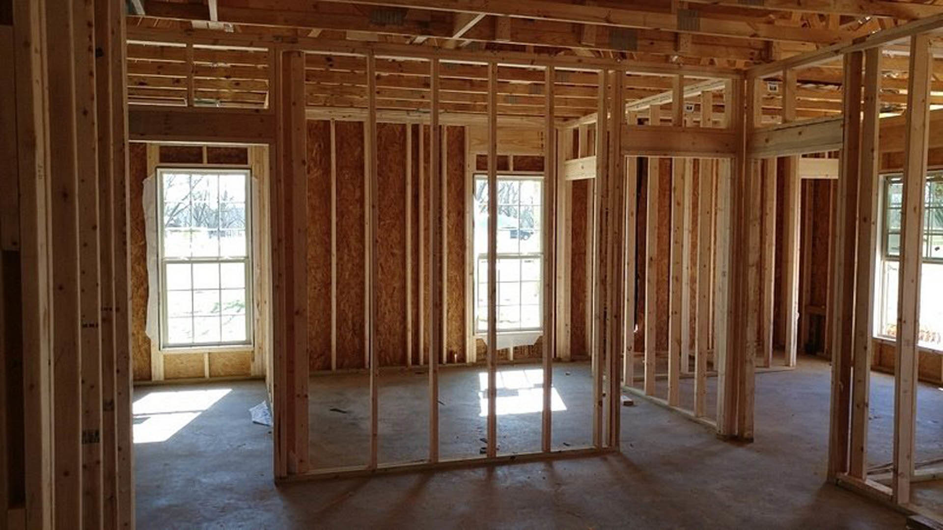 Room with exposed wood framing, ceiling beams, white-framed window, unfinished floor, and view of a car outside