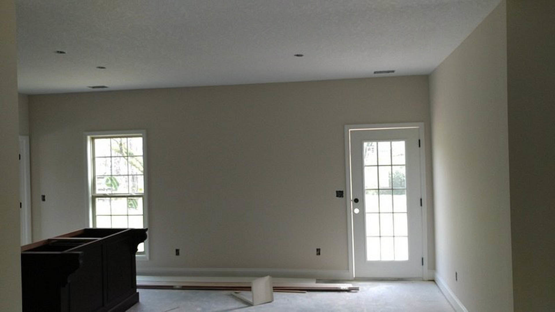 White-walled room featuring a black upright piano, dark wood cabinet with open shelf, white door with glass panes, and a window with white trim.