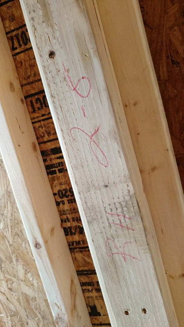 Wooden plank with handwritten red markings on natural grain surface