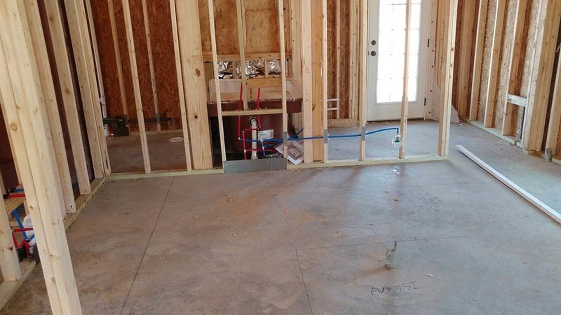 White door with glass panels, concrete floor, wall opening, long white wood plank, sink, and tub in a partially finished room with exposed insulation and laminate flooring.