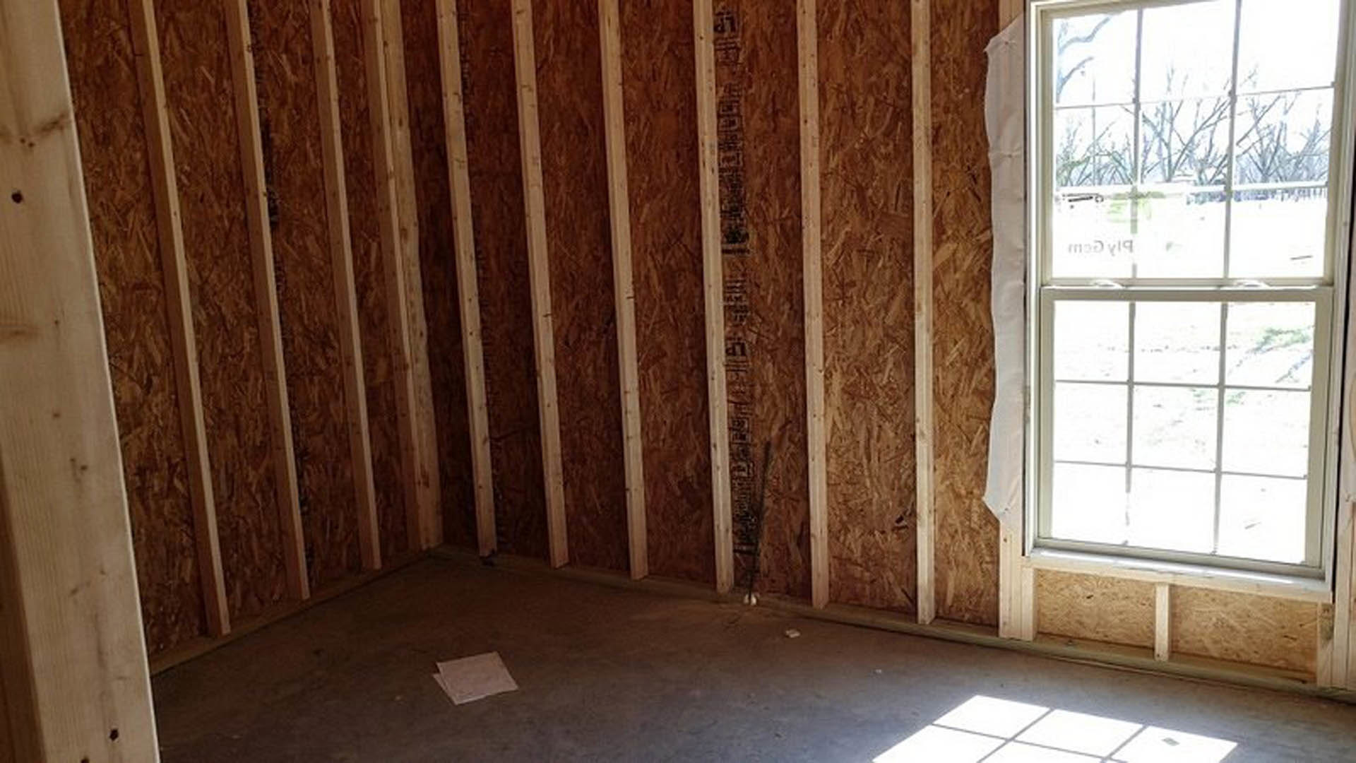 Large window with sheer white curtains, snowy landscape visible outside, stone accent wall, concrete floor, wooden ladder leaning against wall