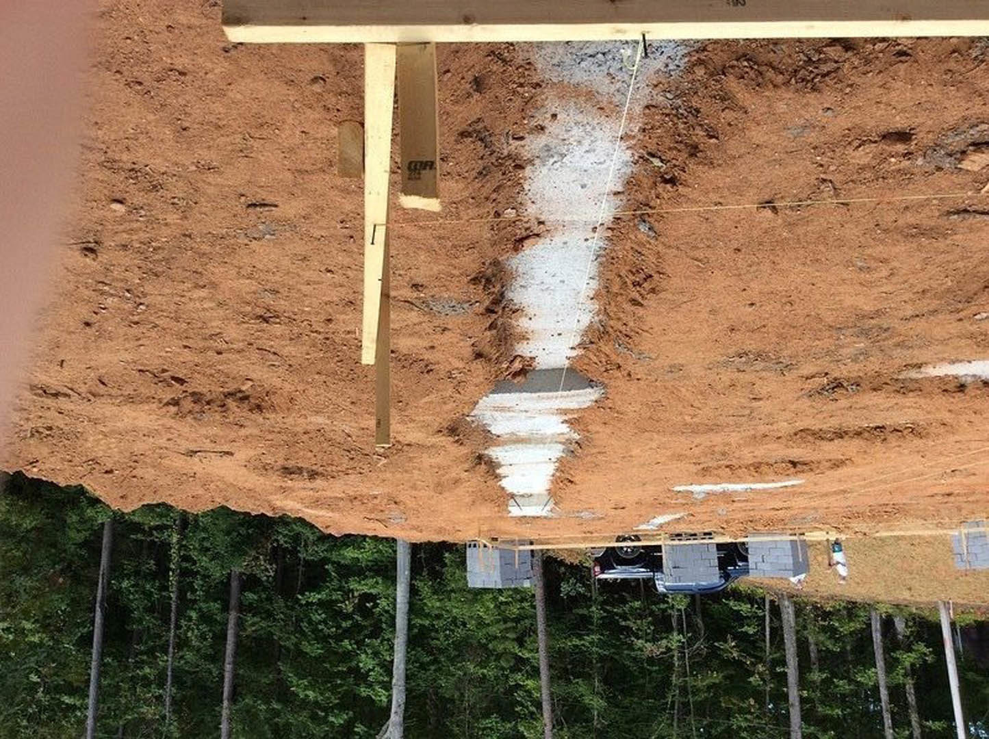 Exposed wooden beam set on a dirt hill with sparse vegetation, surrounded by outdoor landscape and trees in the background