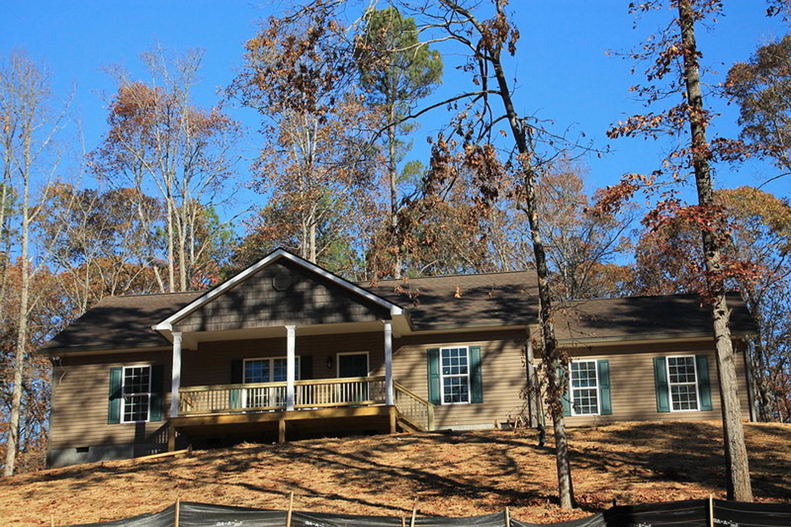 Two-story house with white siding, multi-pane windows, and a covered porch, situated on a grassy hill with trees in the background