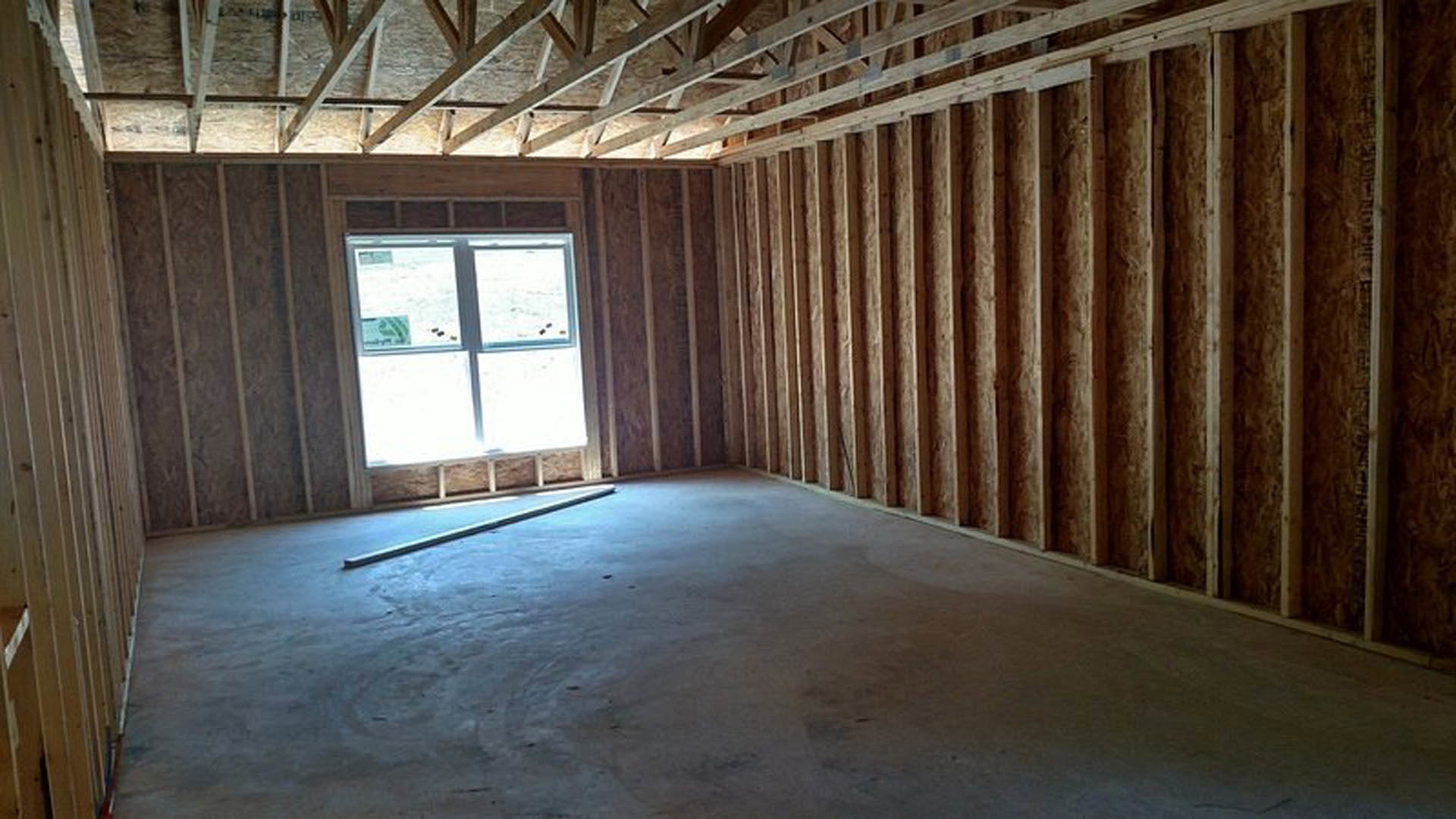 Concrete floor and exposed wood ceiling beams in a room with a large white-framed window, neutral walls, and natural daylight.