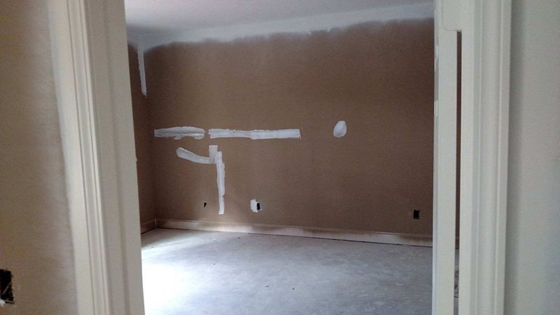 Brightly lit room with smooth white painted walls, light-colored plaster ceiling, wood flooring, and a simple door with a metal handle