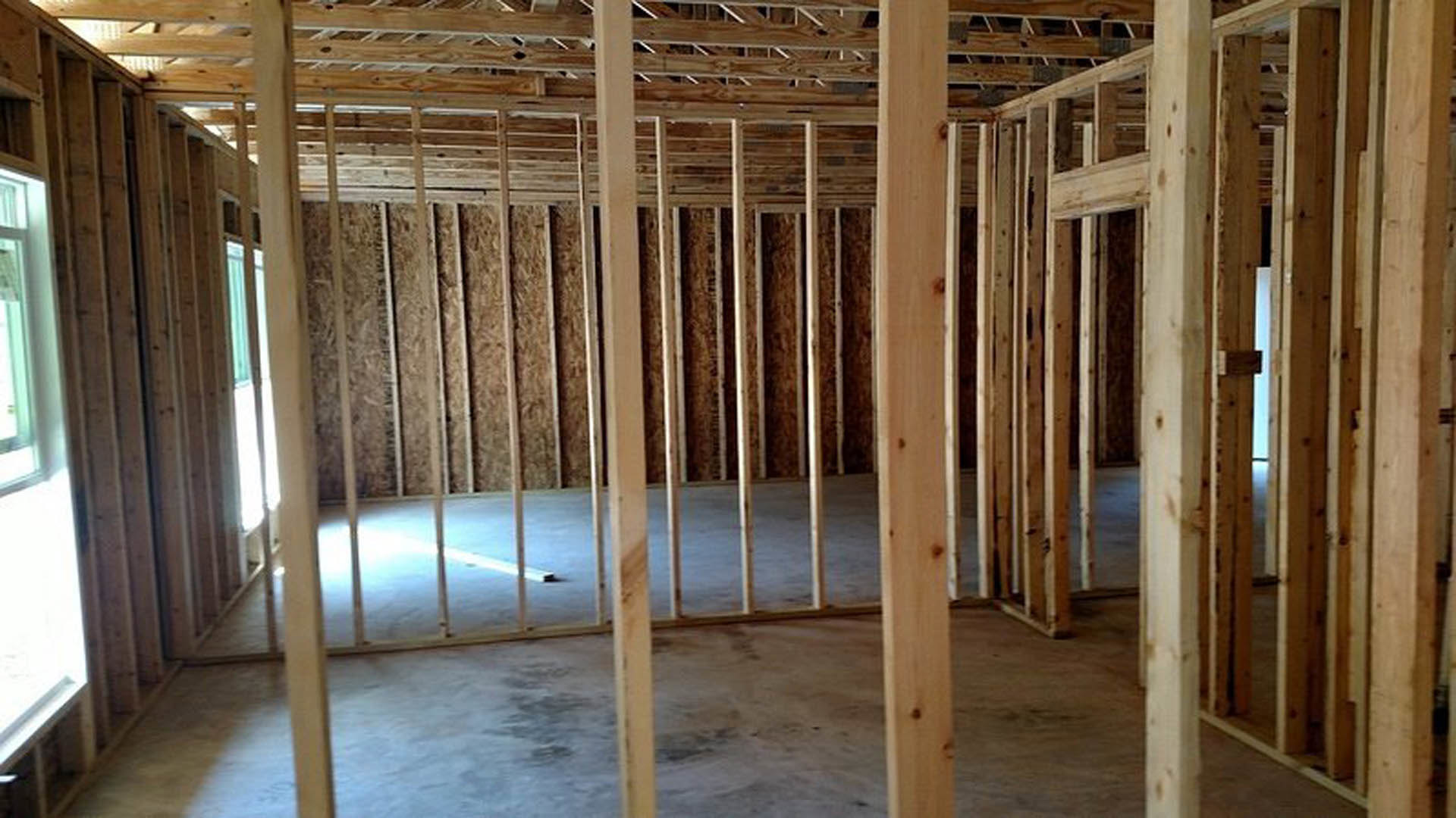 Room under construction with exposed wood framing, ceiling beams, unfinished walls, and concrete floor