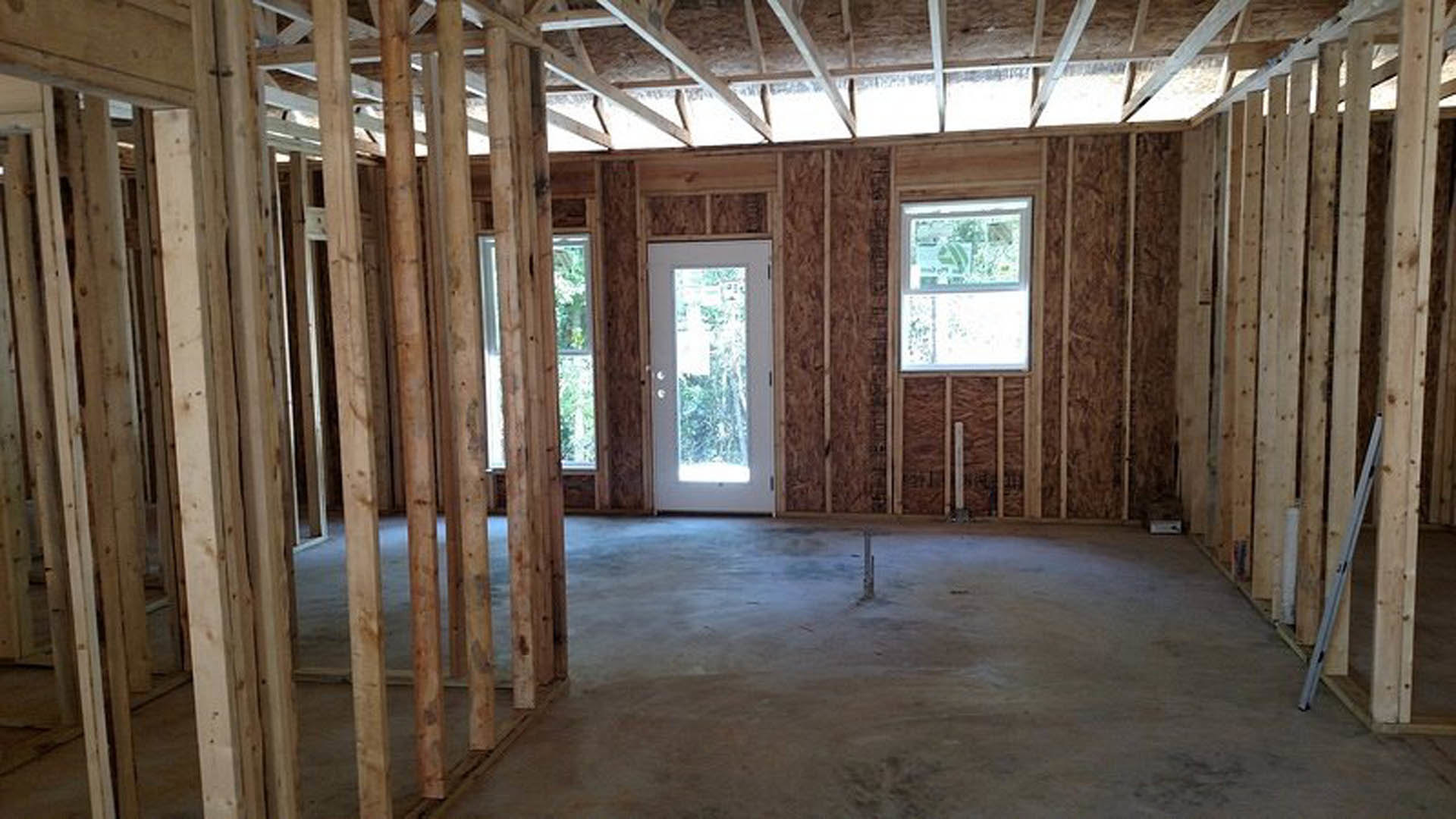 Room with exposed wooden ceiling beams, white framed window, and white door with glass insert, light-colored walls and flooring