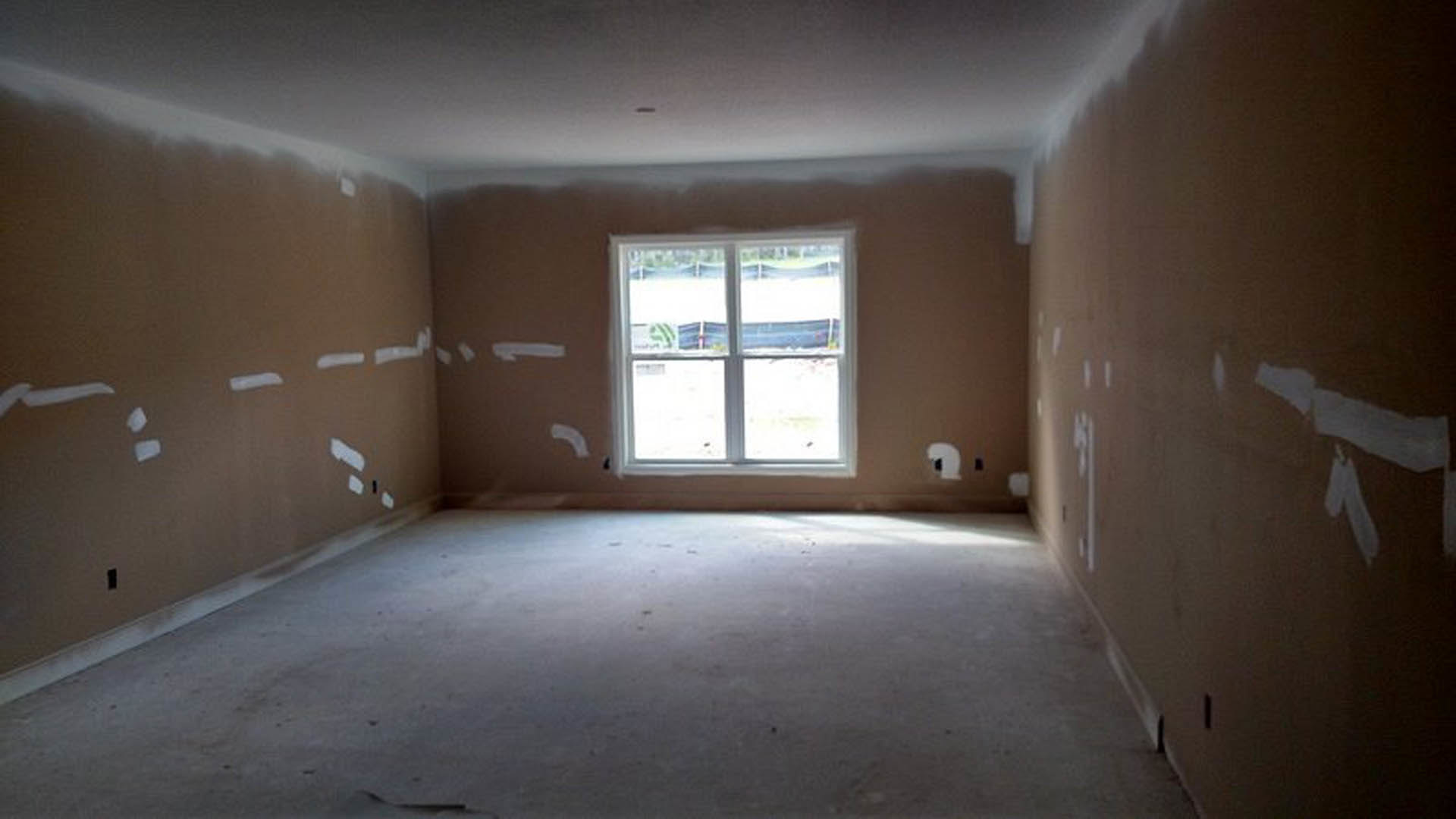 Sunlit room with a white-framed window, smooth plaster walls, concrete floor, and hallway featuring white tape accents and modern light fixtures.