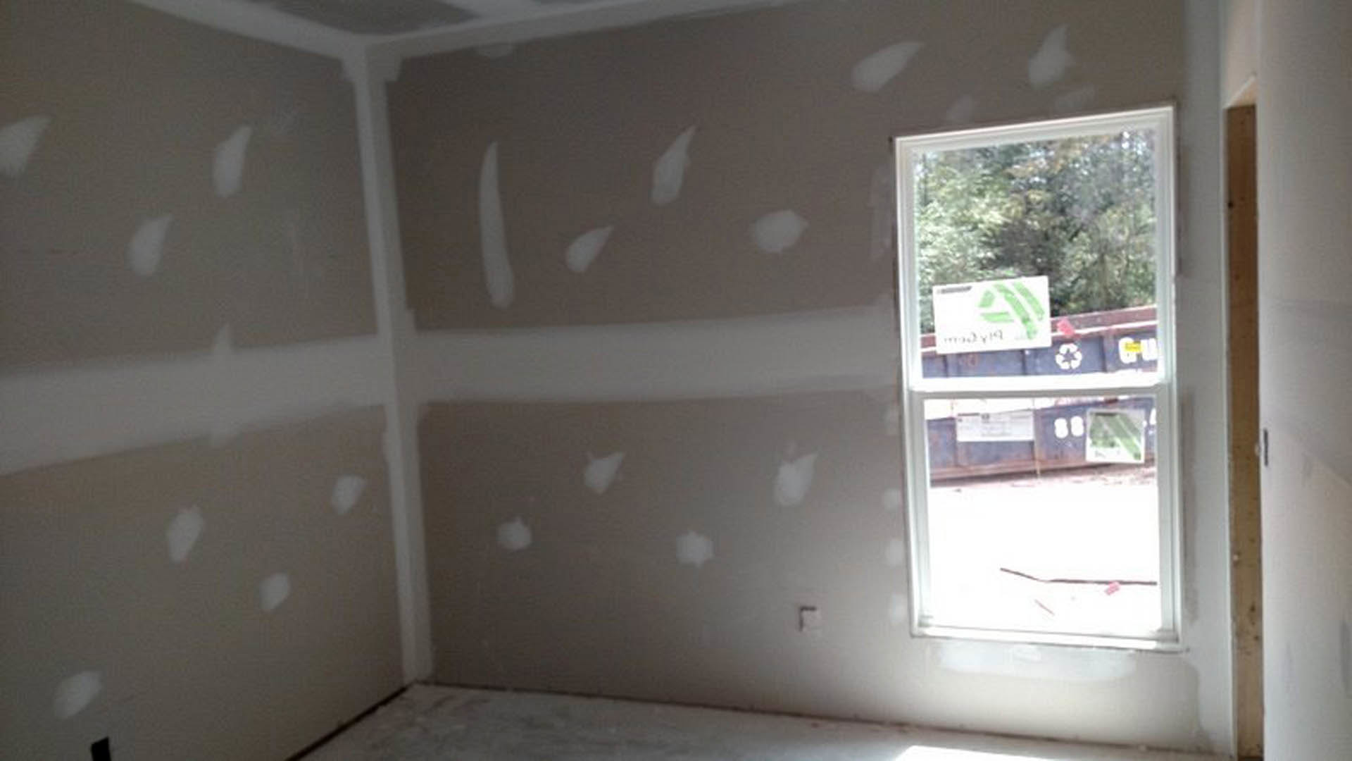 White-walled room with a large window, light-colored flooring, and simple ceiling trim